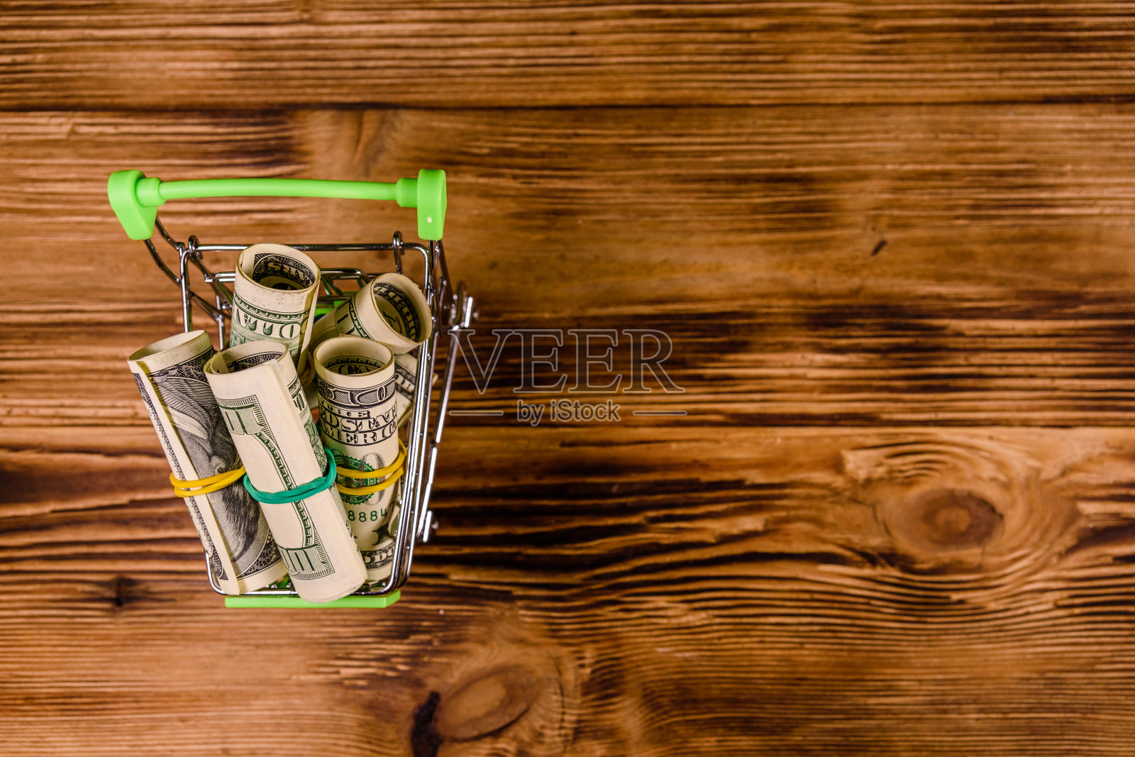 木制背景上的小购物车,上面是卷起的一百美元钞票。俯视图照片摄影图片