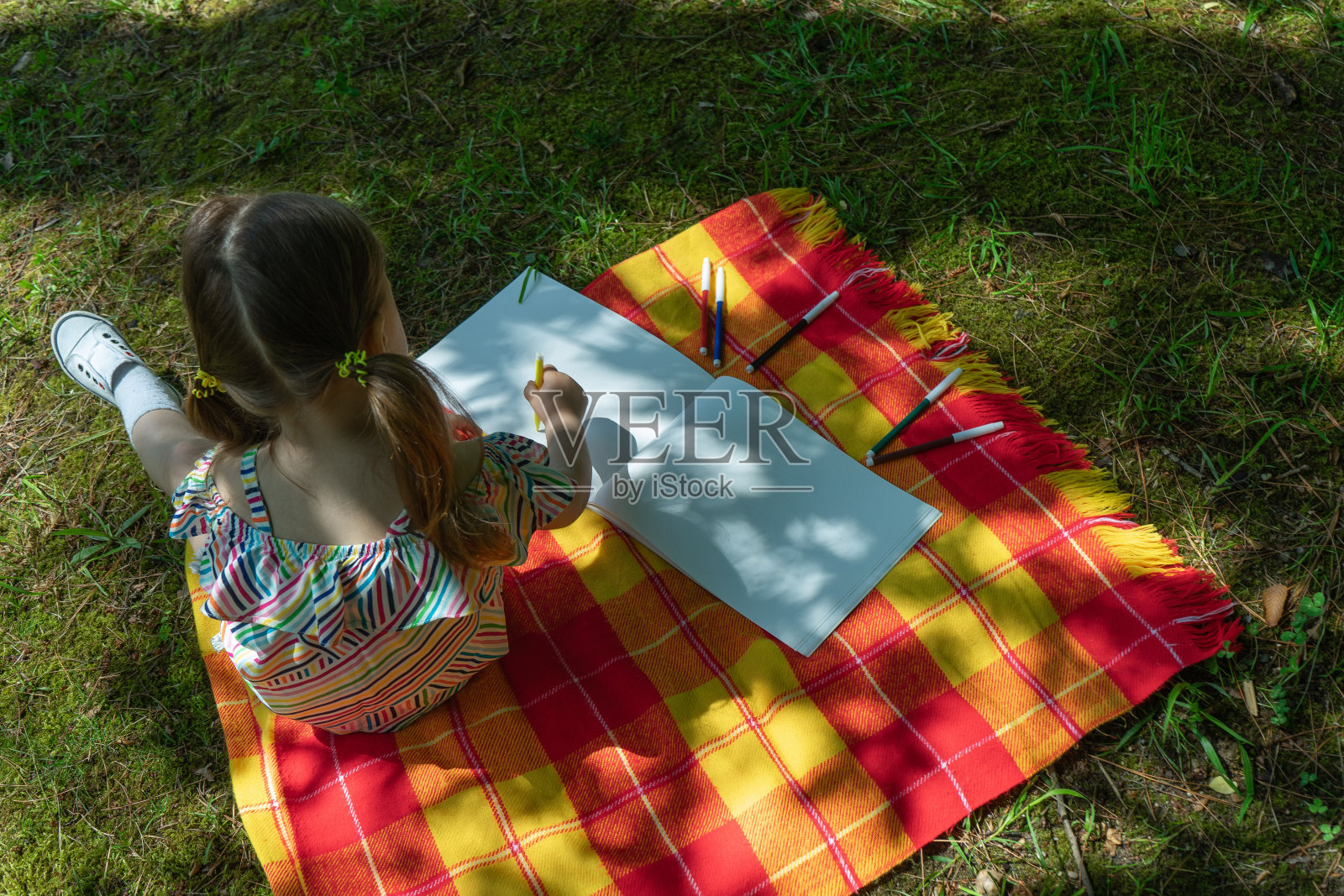 一个蹒跚学步的小孩正在户外用彩色毛毡笔画画。照片摄影图片
