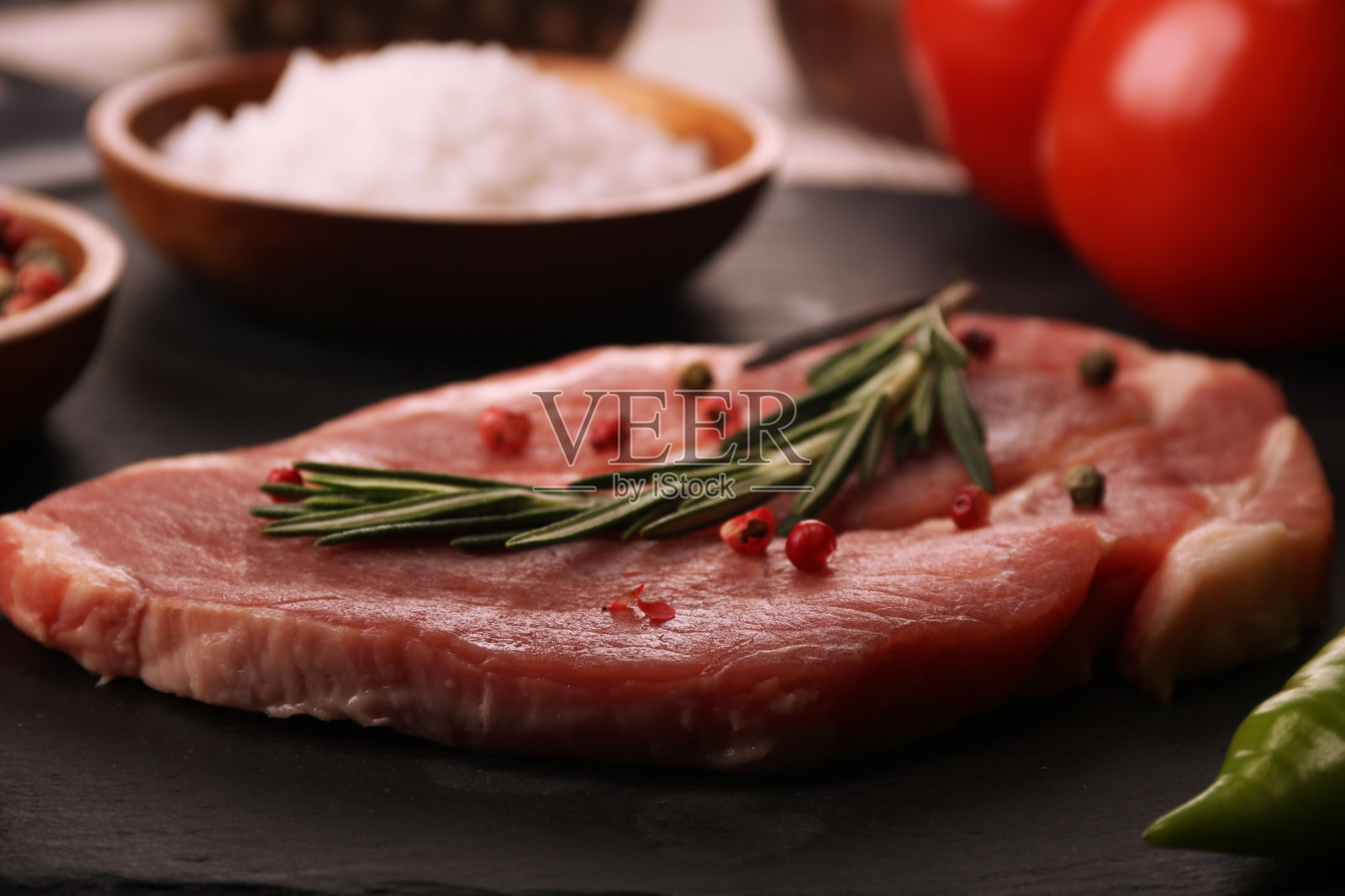 生猪肉排配蔬菜、辣椒、番茄、盐、迷迭香和香料在石桌上烹调。照片摄影图片