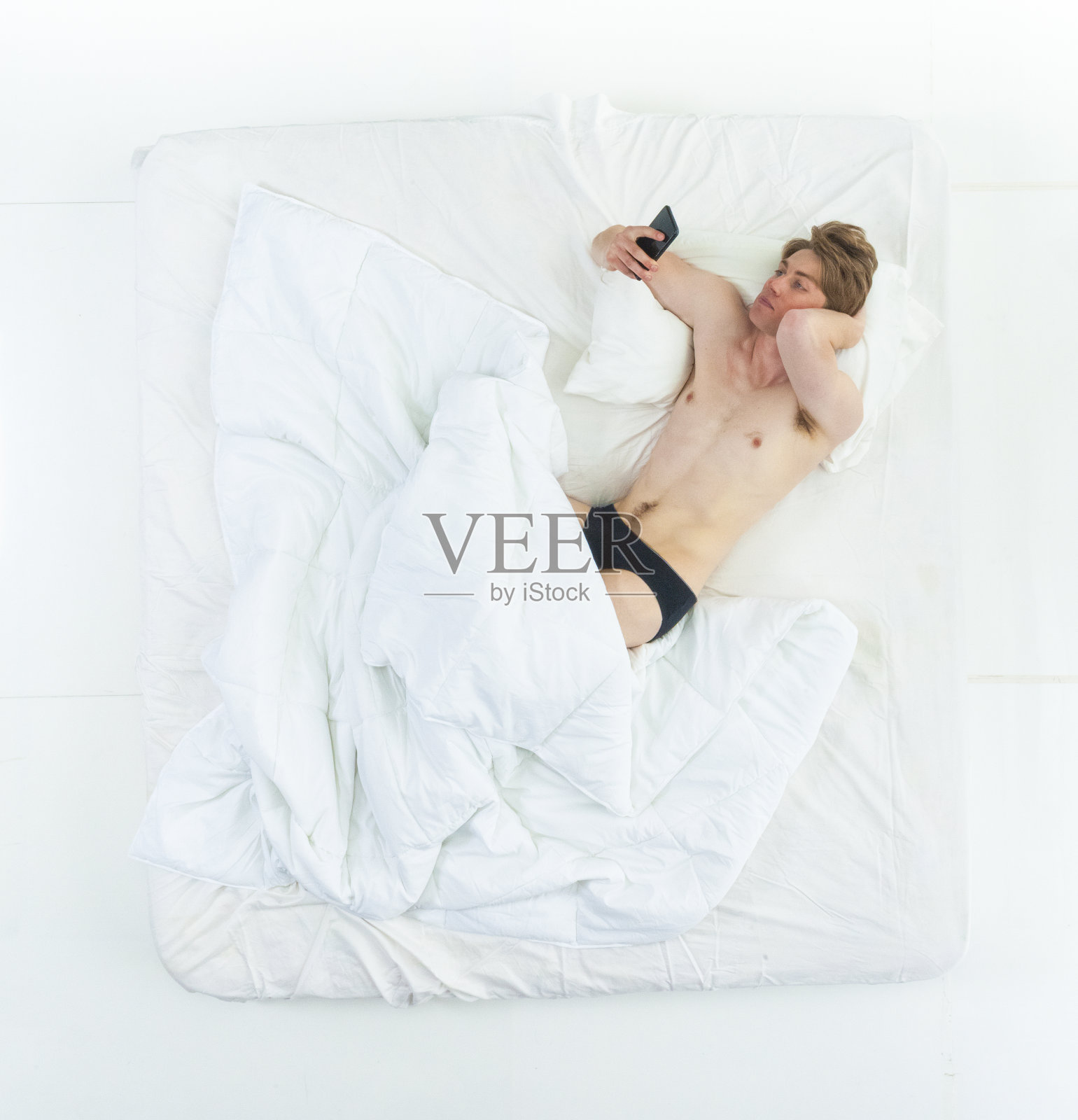 英俊的男人躺在床上,赤膊上阵,还在打电话照片摄影图片