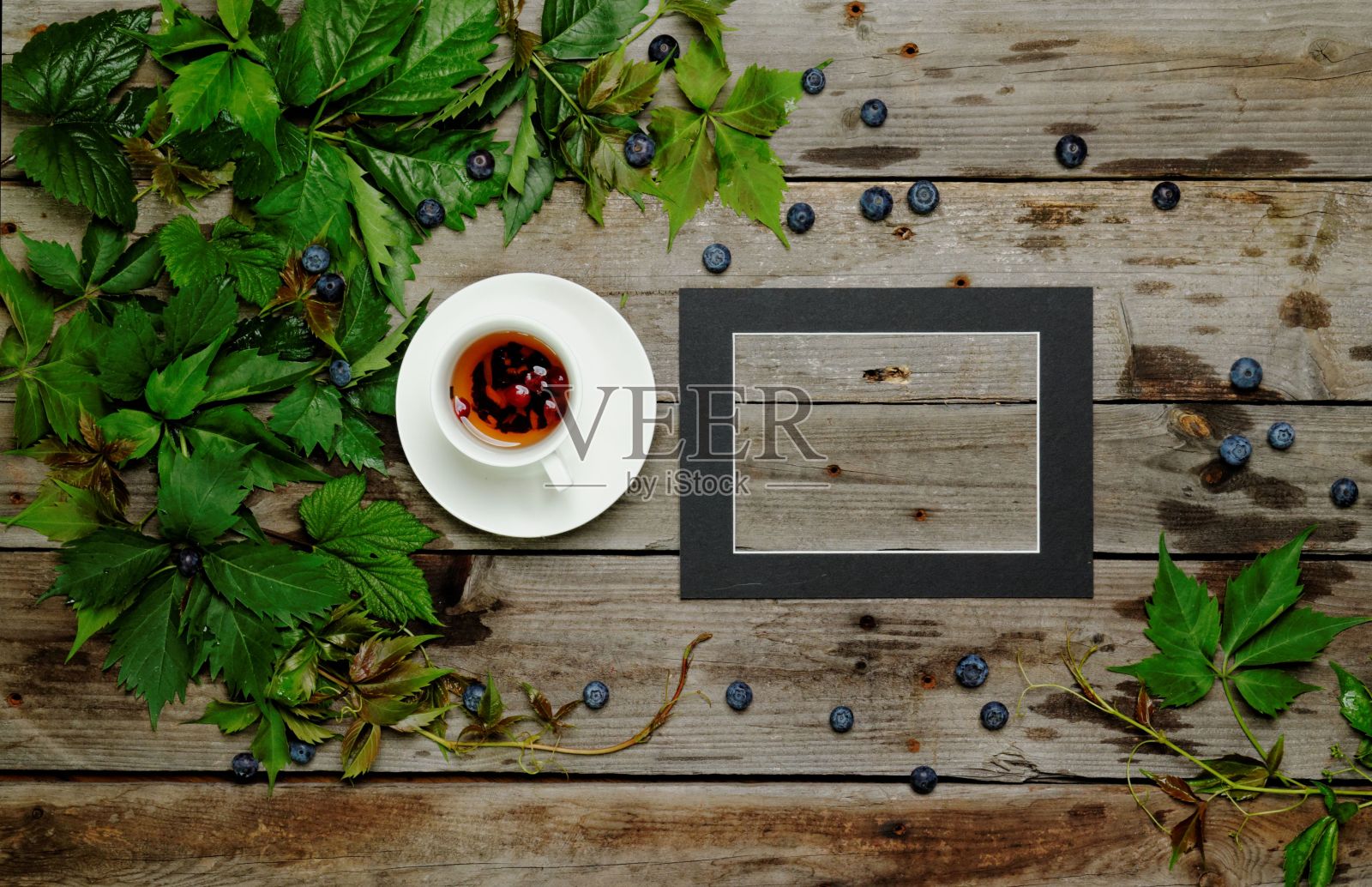 俯视图杯茶和钢笔与空的画框在木制的背景与绿色的叶子和浆果照片摄影图片