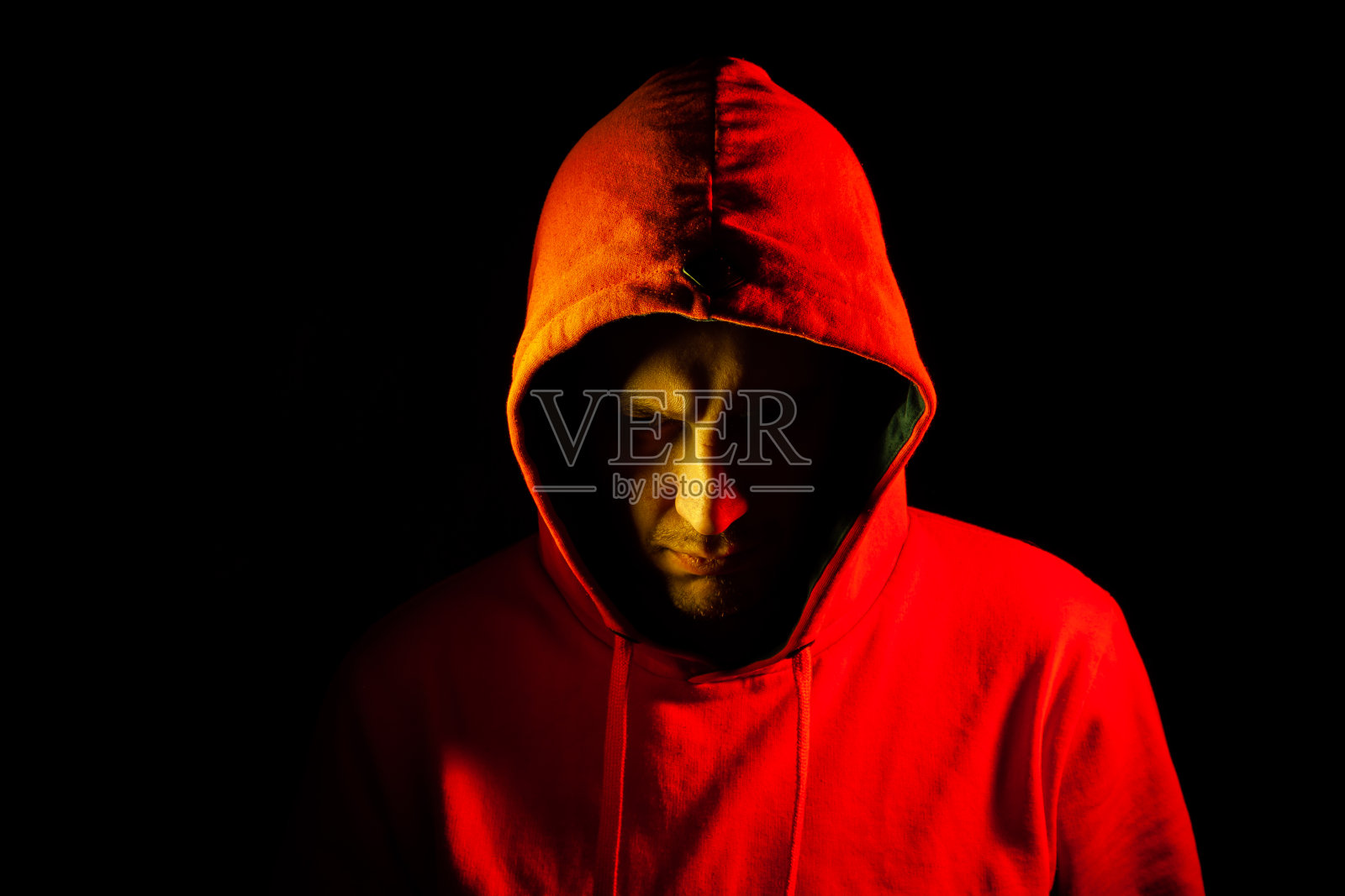 特写的一个人的头在一边的橙色兜帽和看下与一个黄色的背光。在与深思的目光战斗前的感觉。脸的一部分被阴影遮住了照片摄影图片