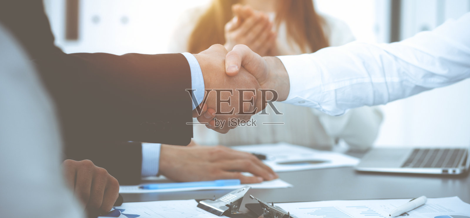 商务人士在会议上握手,而他们的同事在鼓掌和鼓掌。一群不知名的商人和妇女在现代白人办公室。成功的团队合作、伙伴关系和握手理念照片摄影图片