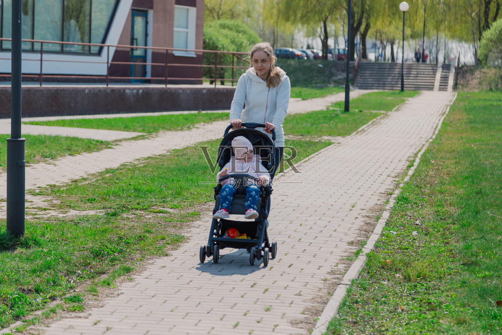 夏日公园里,年轻的母亲推着婴儿车抱着孩子照片摄影图片