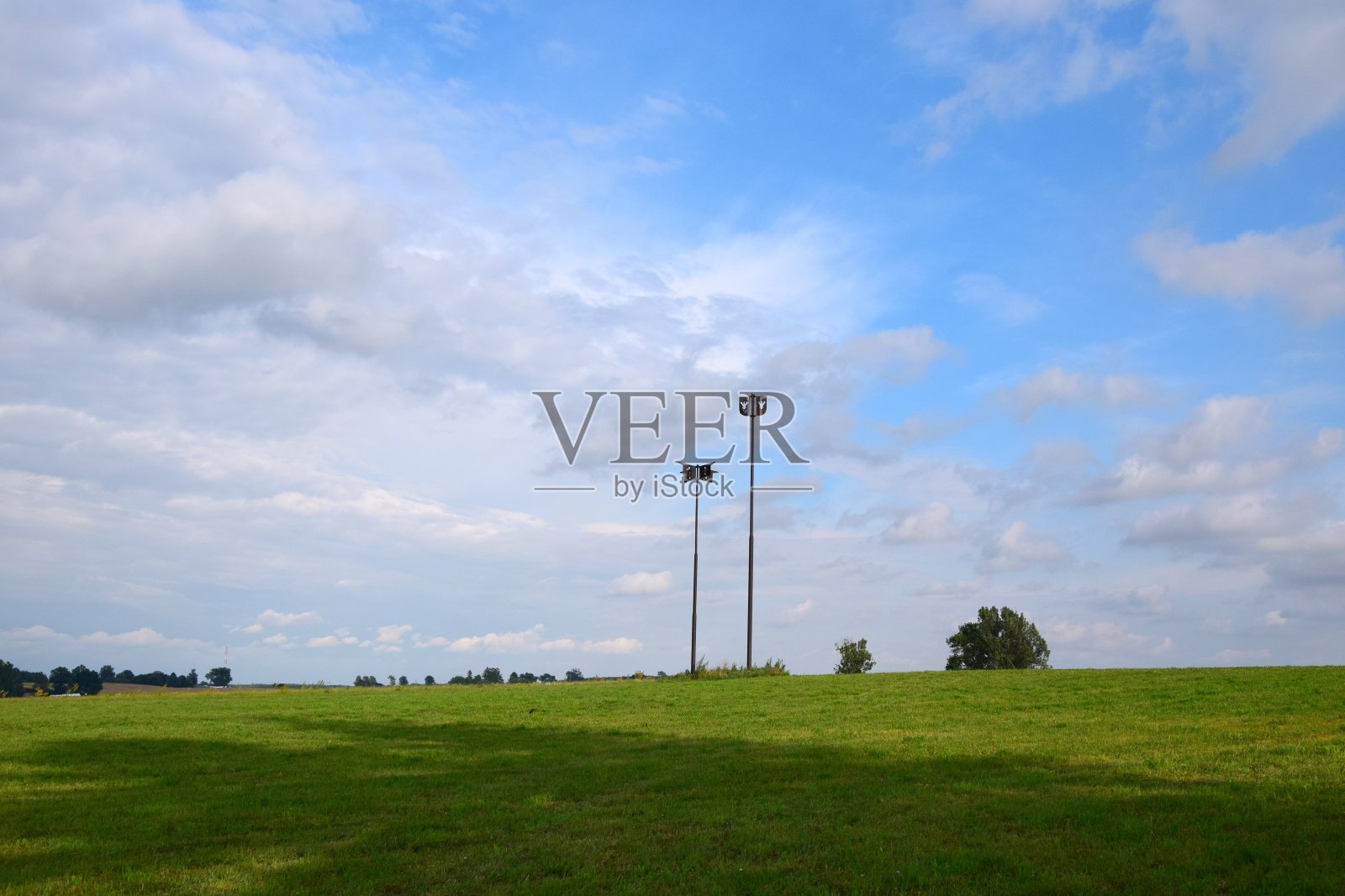 两个金属纪念碑高耸在夏日的天空中,一个更高,一个更小,前景是一个巨大的牧场或农场,背景是两棵树,上面是一团团的云照片摄影图片