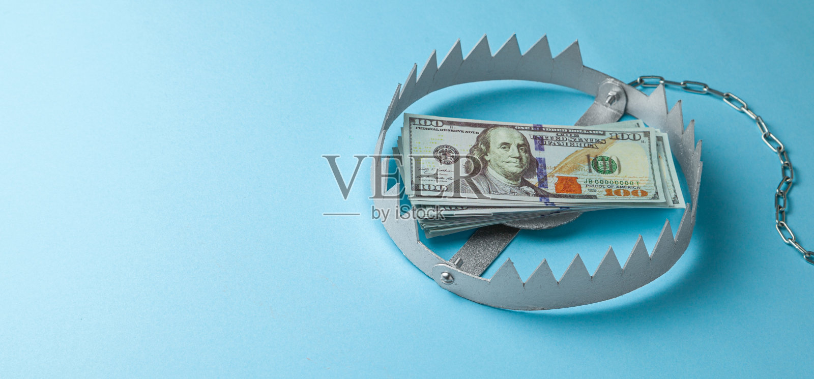 用一堆钱设陷阱。投资或商业欺骗的危险风险。蓝色背景。照片摄影图片