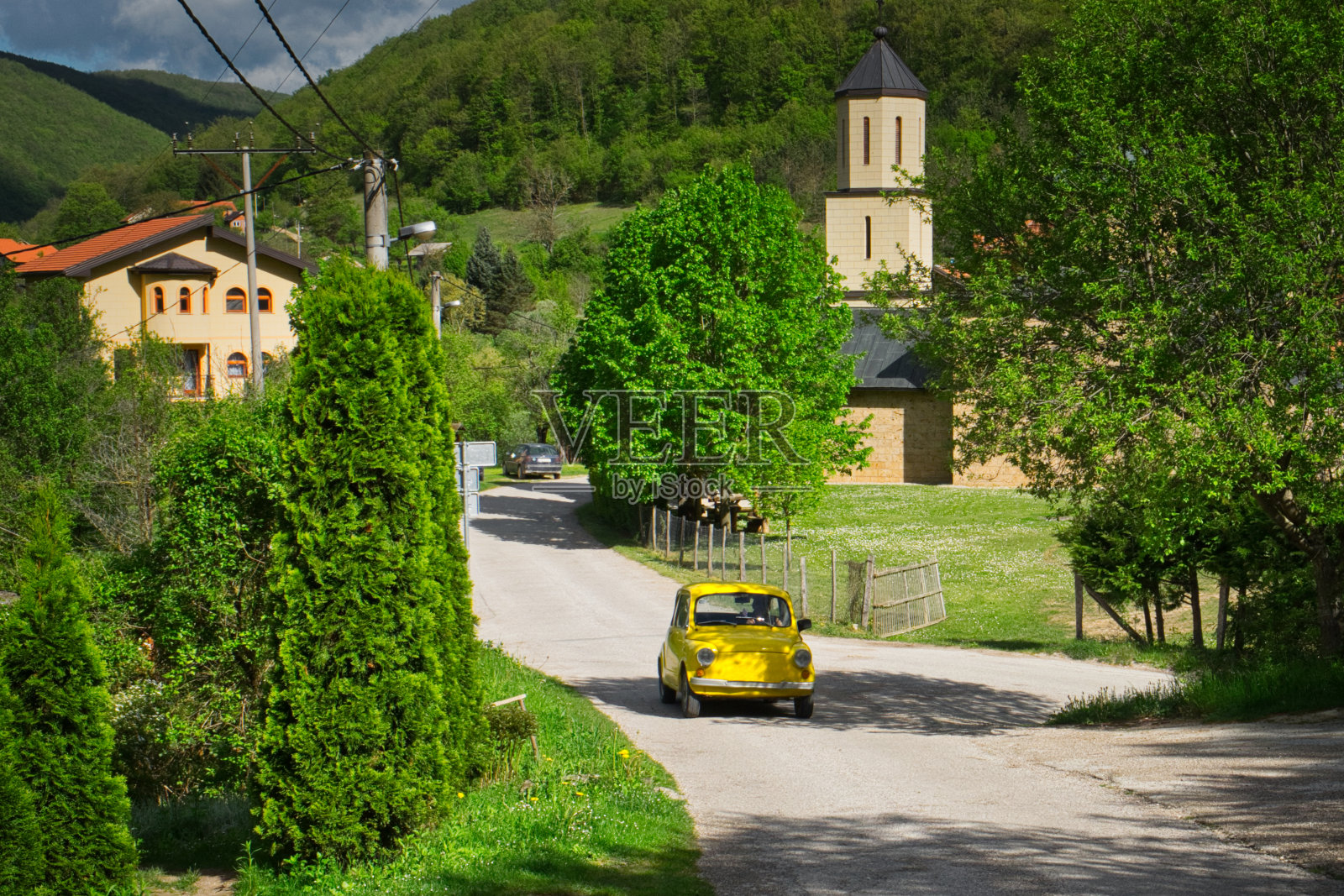 在一个阳光明媚的日子里,一辆黄色的旧车行驶在波斯尼亚和黑塞哥维那绿色山谷的乡村道路上照片摄影图片