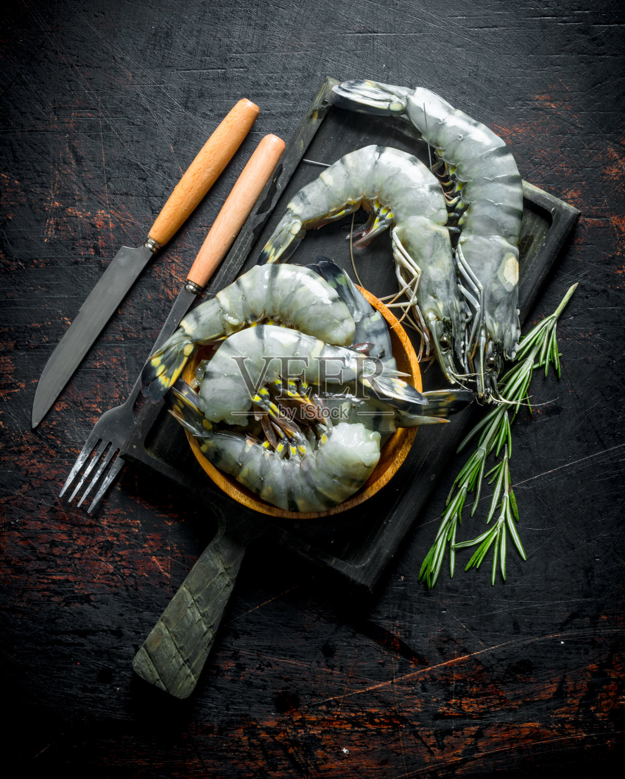 生虾和迷迭香放在砧板上。照片摄影图片