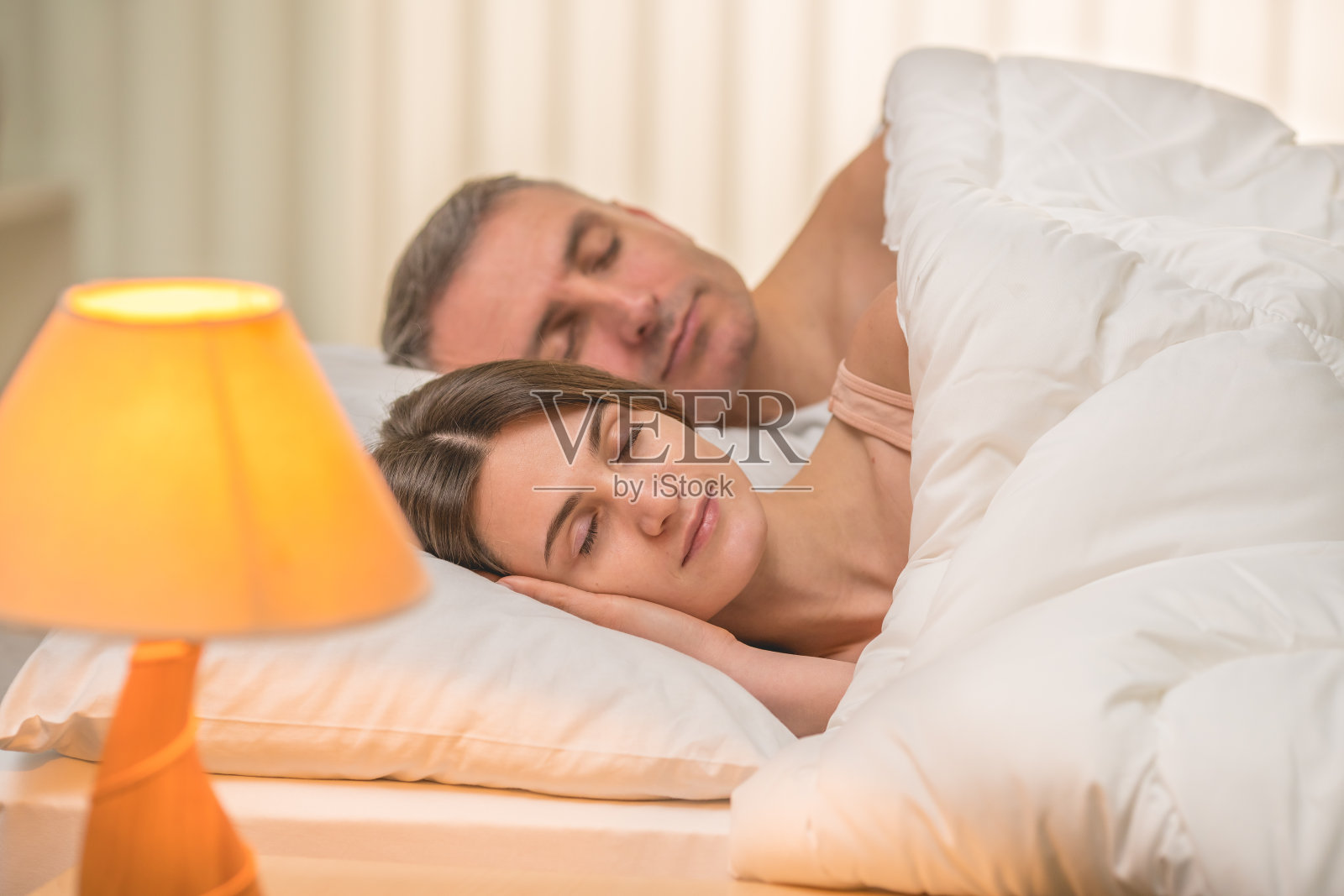 在床头灯的背景下,一对美丽的夫妇睡在床上照片摄影图片