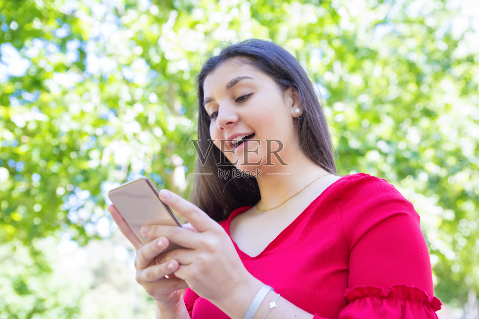 在公园里玩智能手机的年轻快乐女人照片摄影图片