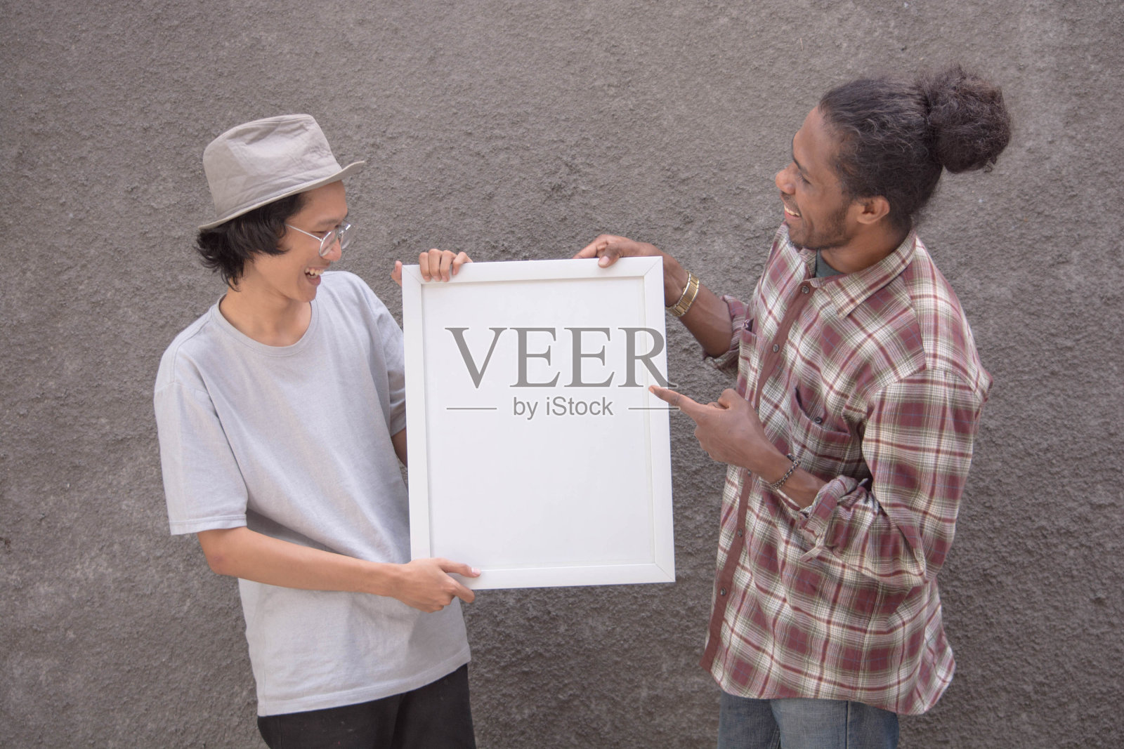 两个不同种族的年轻人指着白板上的空白看着相机,亚洲人和黑人男子拿着白色的框架为拷贝空间在一起照片摄影图片