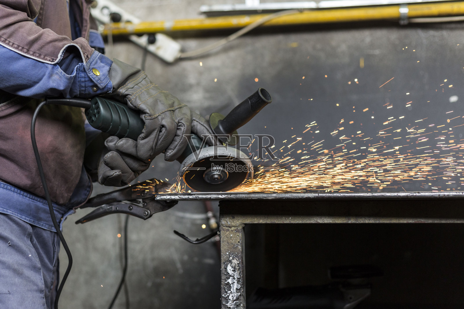 一个戴着面具和手套的工人正在用研磨机打磨一个金属物体。他穿着防护服。照片摄影图片