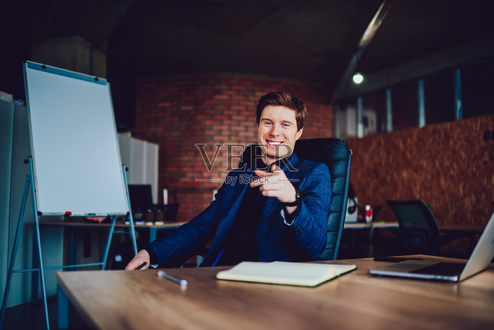 成功的男导演坐在桌面看着镜头,享受快乐的心情,积极的商人在正式穿着花时间在公司办公室感到兴奋和快乐照片摄影图片