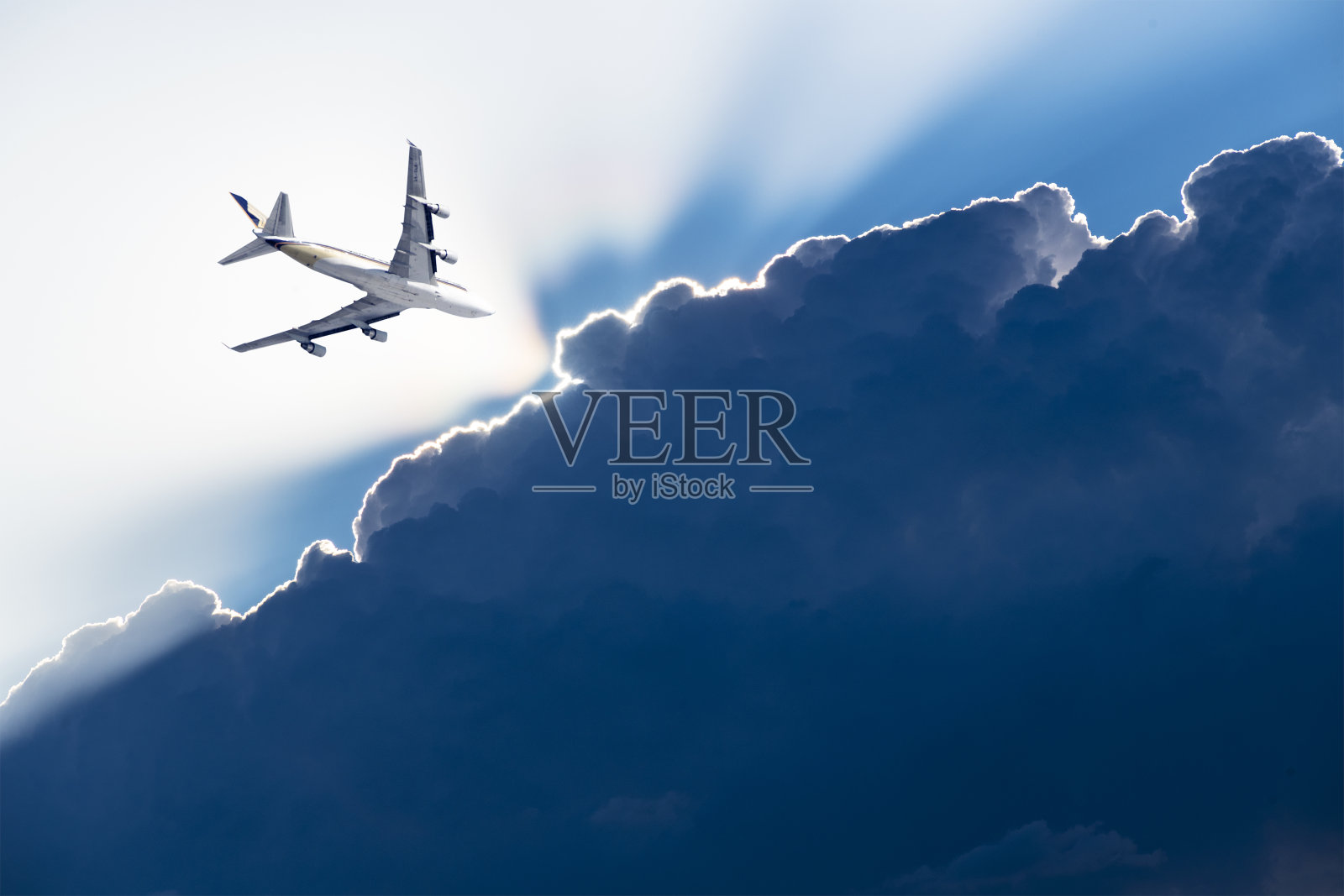 一架飞机在布满乌云的天空中飞行,被阳光穿过照片摄影图片