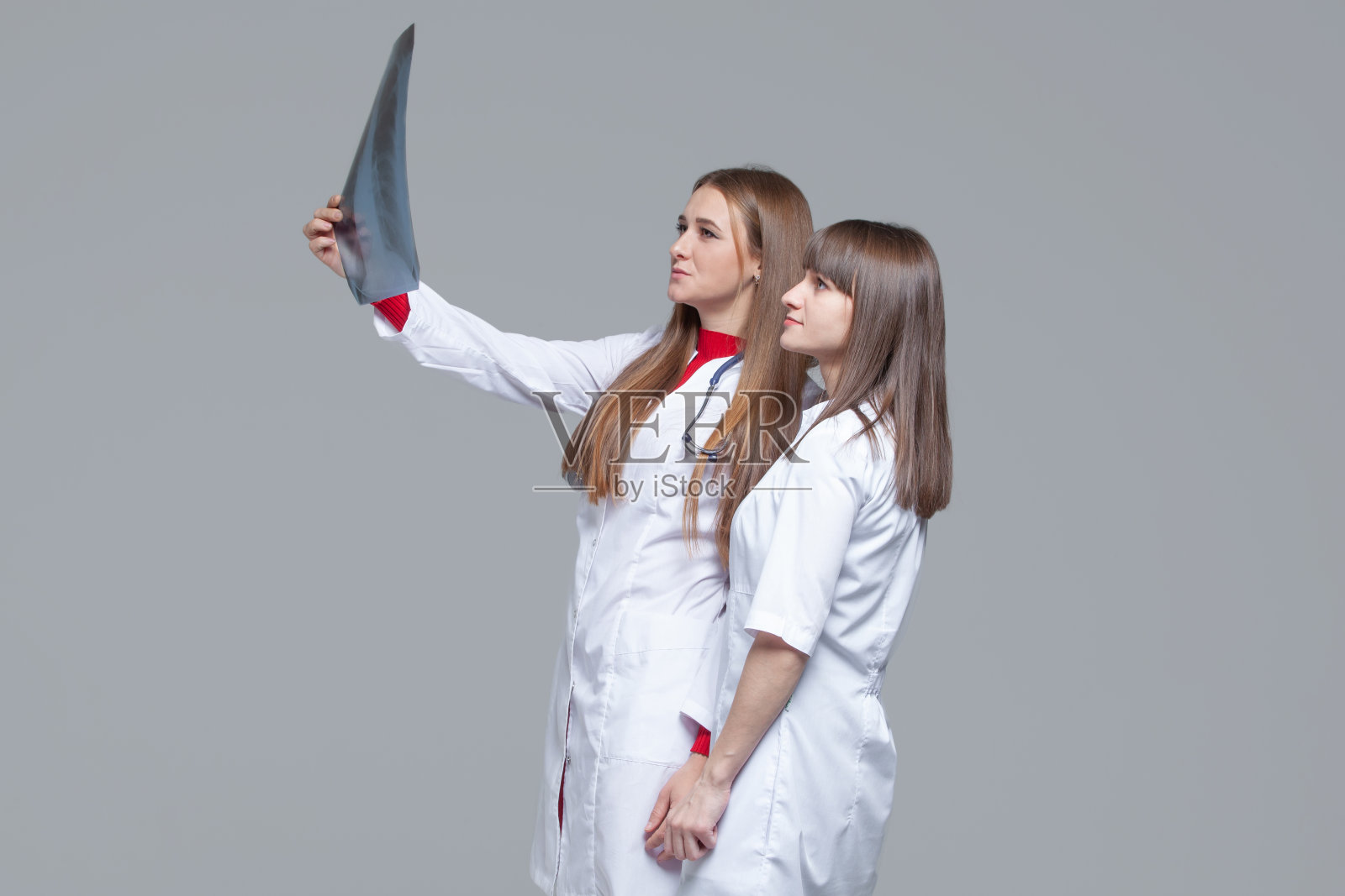 两位年轻的女医生正在看灰色背景的肺部x光照片照片摄影图片