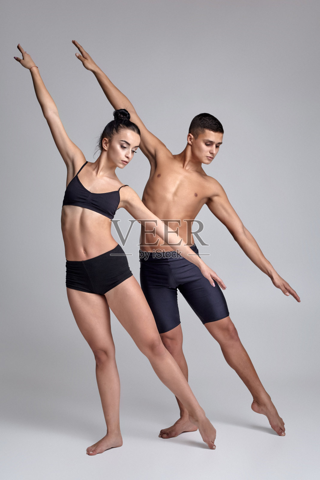 一对穿着黑色西装的年轻现代芭蕾舞者在一个灰色的演播室背景上摆姿势。照片摄影图片