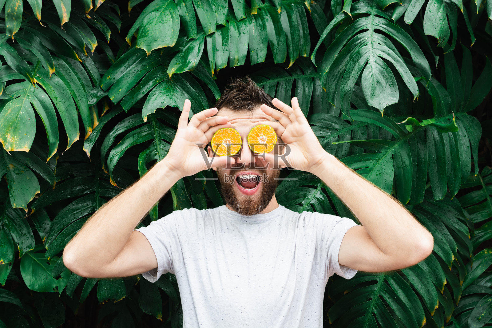 一个留着胡子的年轻人把几片橘子放在眼前,笑着说照片摄影图片