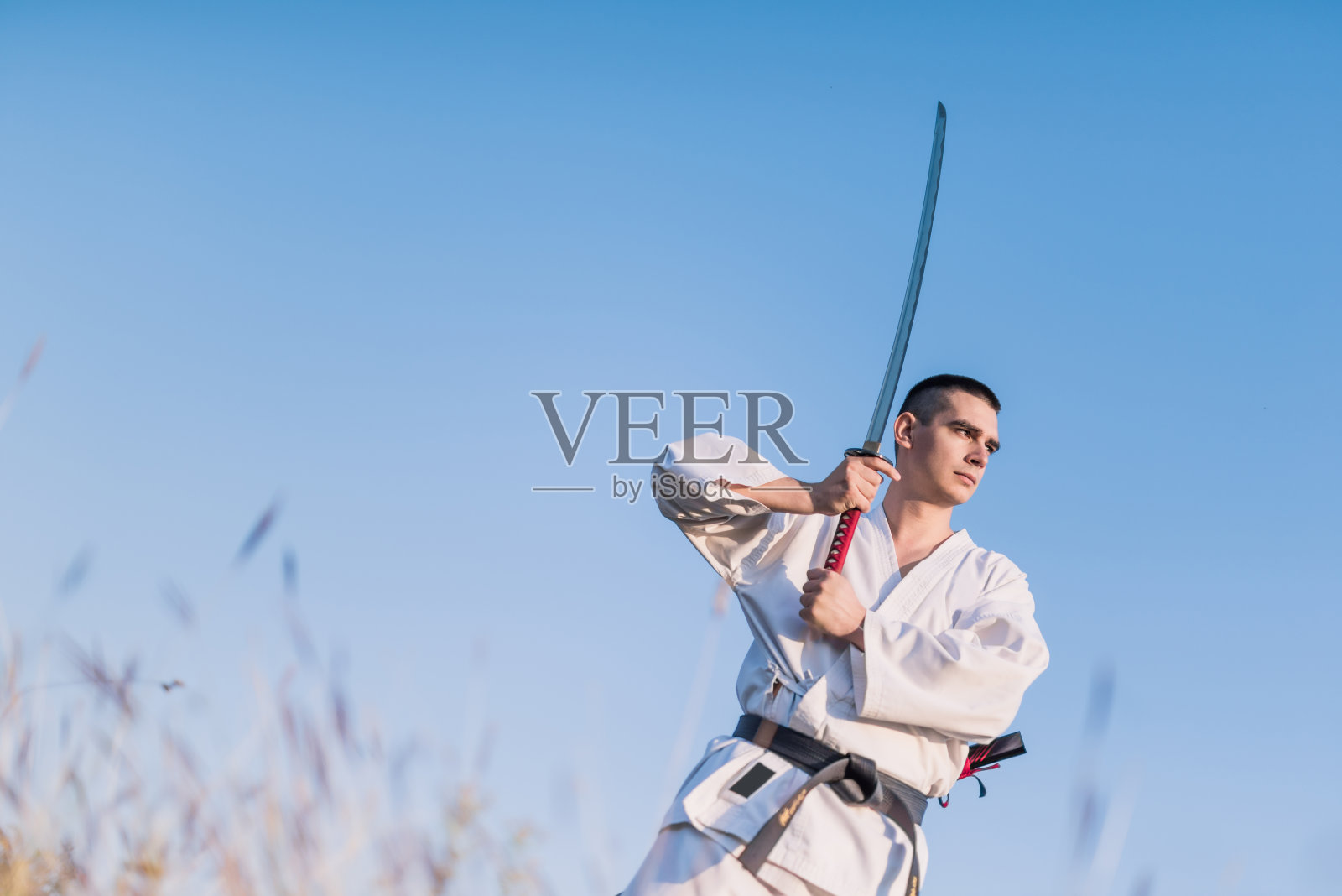 年轻的武术家在户外用武士刀练习技巧。照片摄影图片