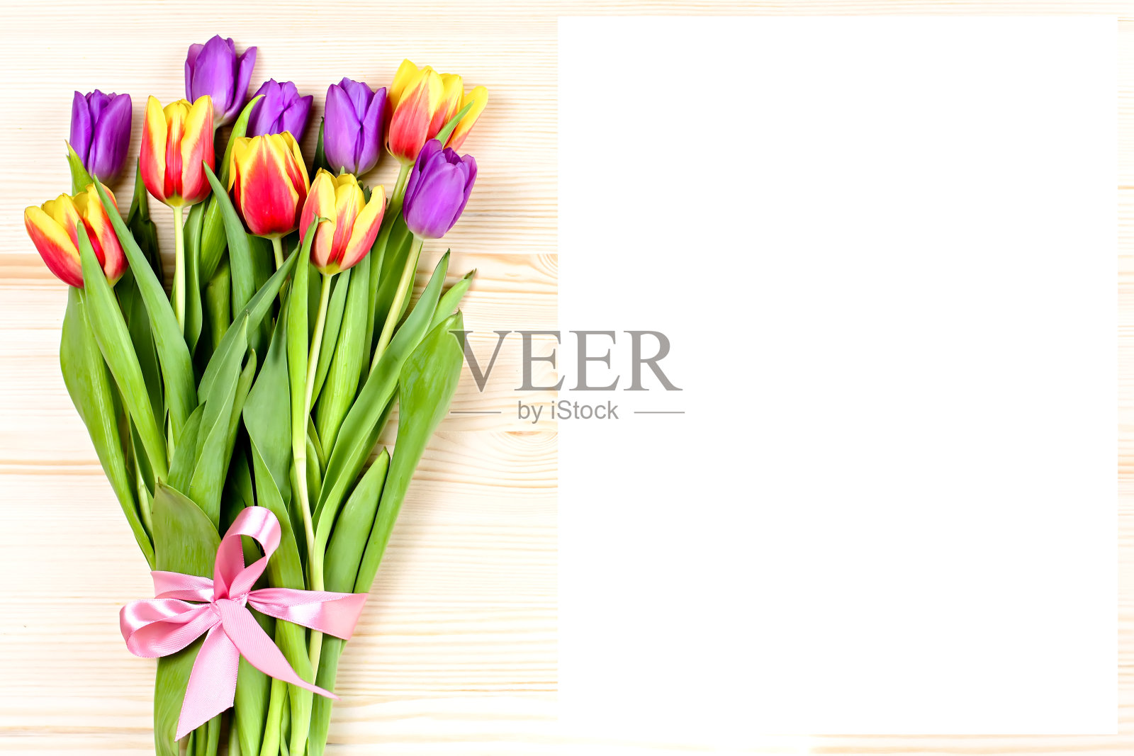 一束色彩鲜艳的郁金香,用丝带装饰在木质背景上。俯视图,复制空间照片摄影图片