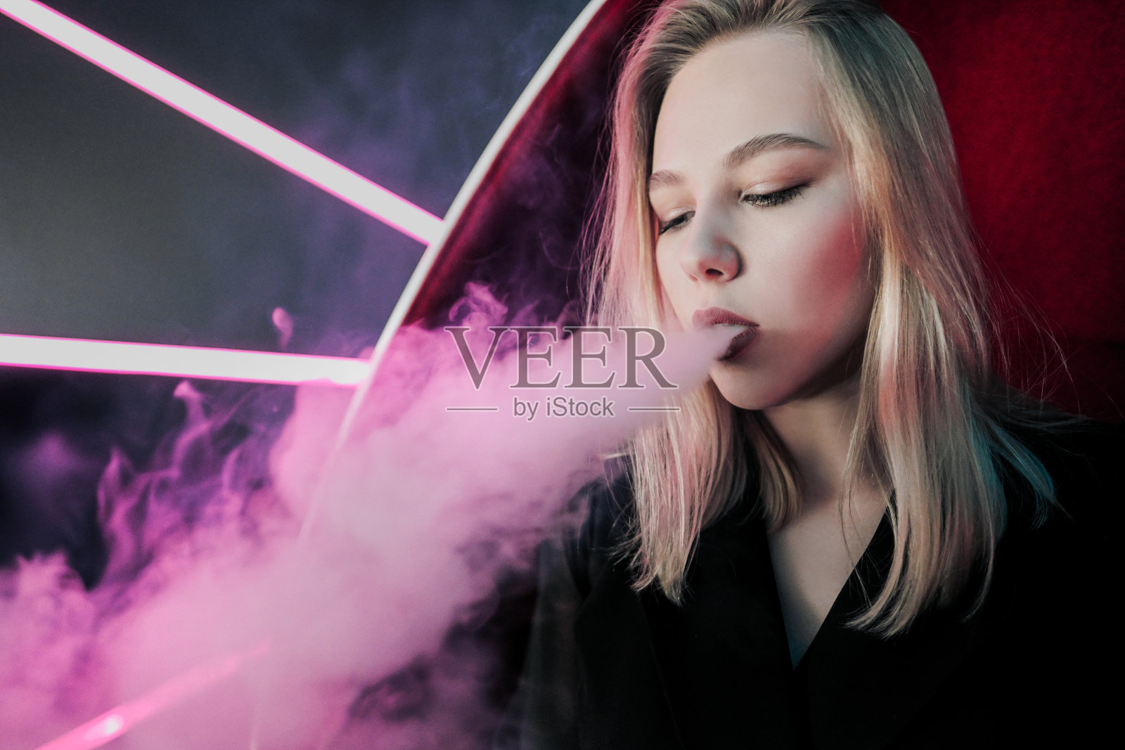 一个漂亮的金发女郎从一个夜总会的水烟管里吐出烟来,背景是紫色的霓虹灯。照片摄影图片
