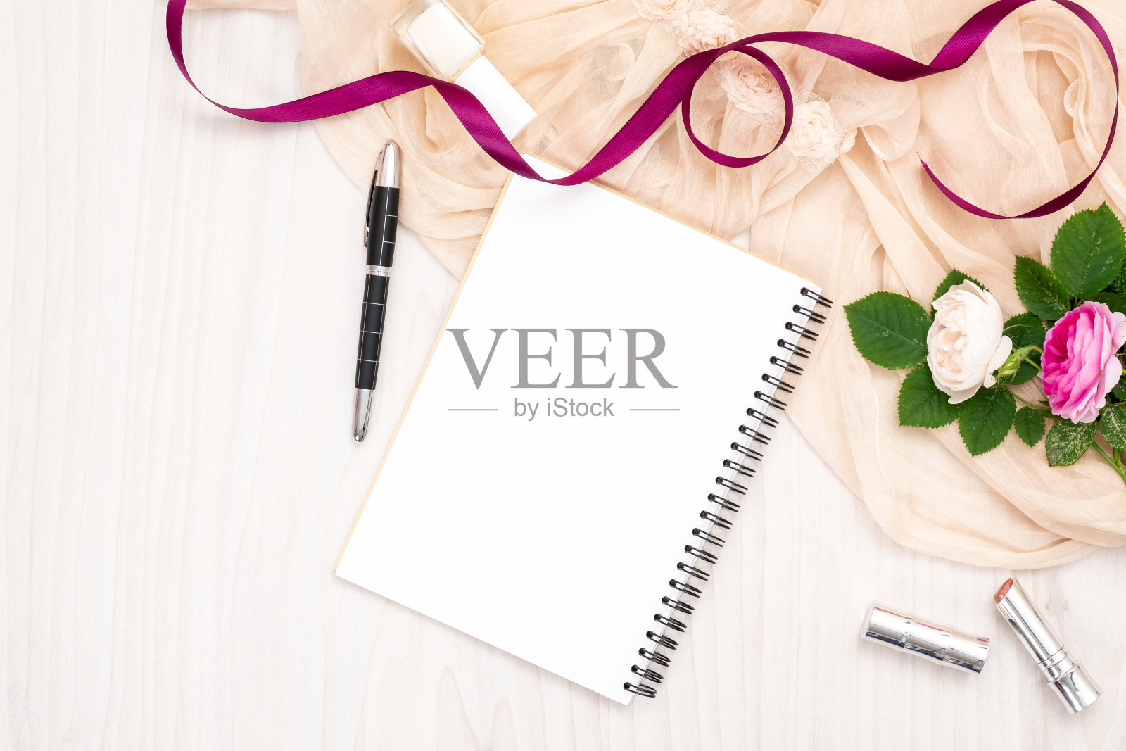 平铺纸笔记本,玫瑰花,丝带,米色围巾,口红在木桌上。俯视女性家庭办公空间,女性背景。时尚博客横幅,美丽和科技的概念。照片摄影图片
