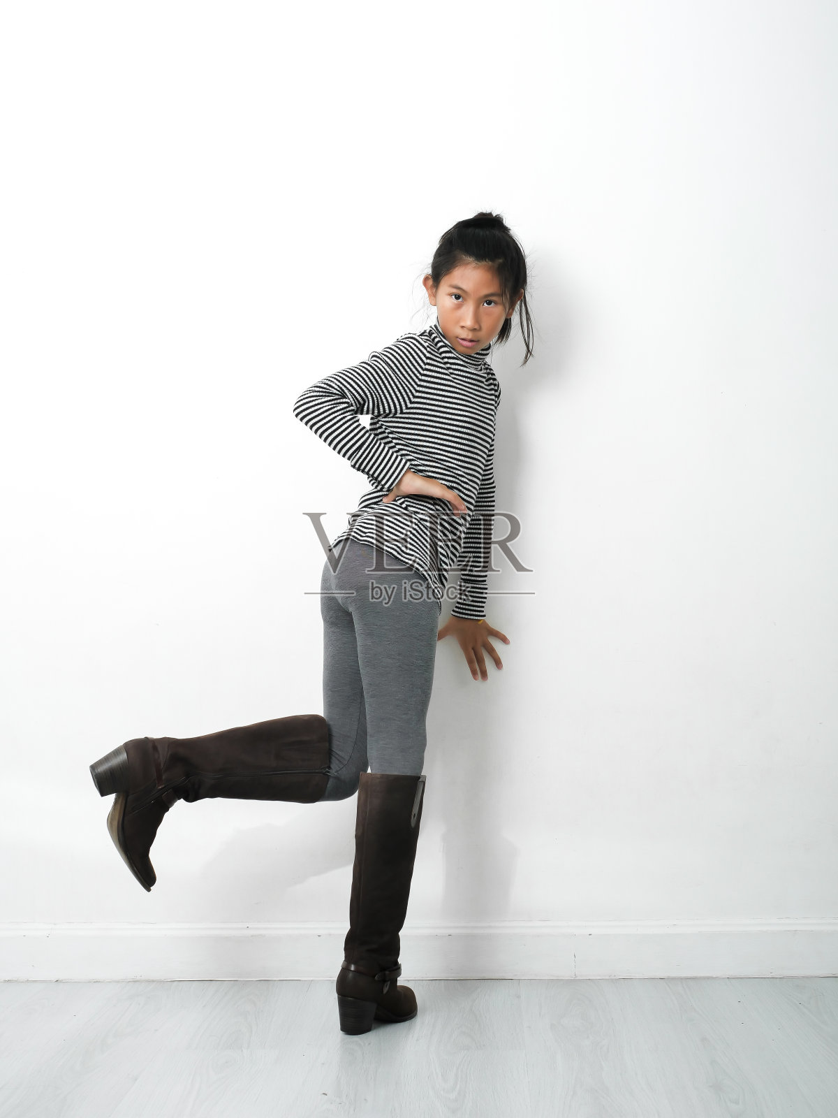 亚洲女孩穿着高领,瘦削和长靴白色墙壁和灰色木地板,时尚概念。照片摄影图片