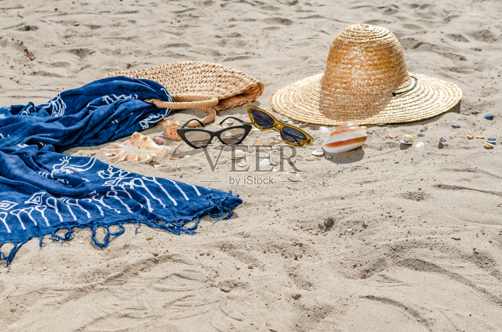 草帽、包、小玩意、太阳镜、贝壳和绿叶躺在沙滩上。暑假的场景。女人的东西照片摄影图片