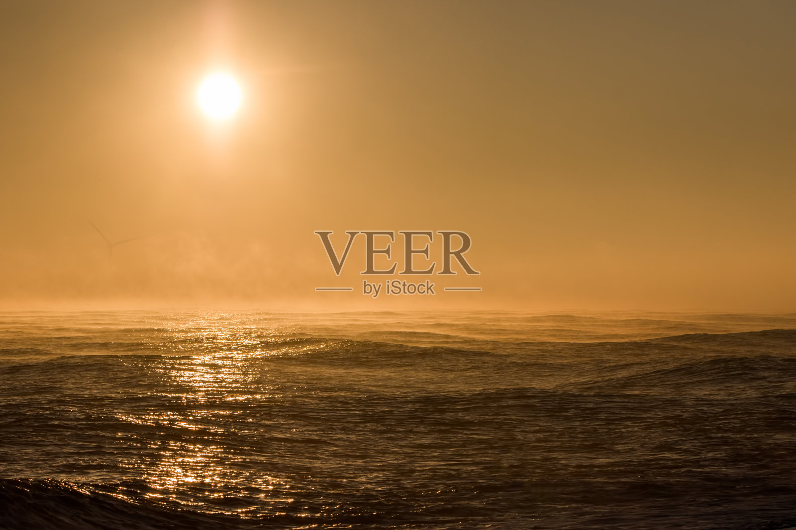 海景日出。美丽的薄雾早晨太阳在海上与背景风力涡轮机。照片摄影图片
