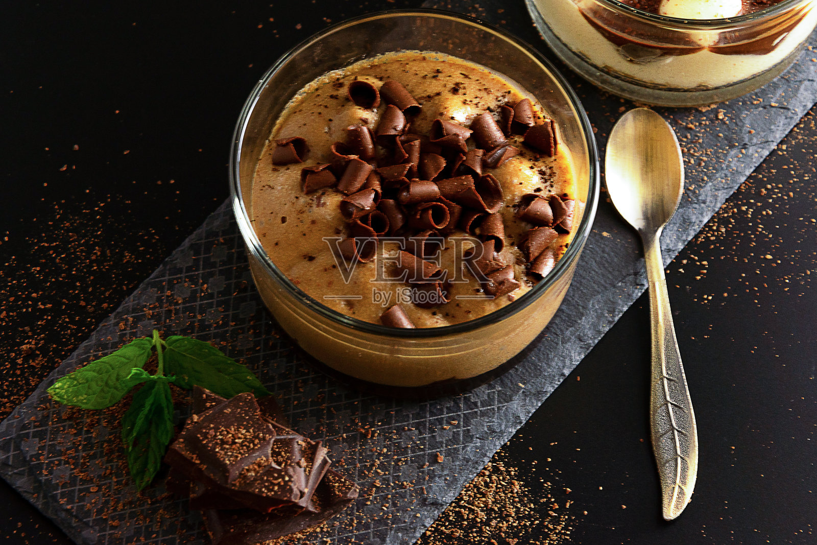 在黑色的背景上,一个黑色的石头盘子上的一个罐子里的摩卡奇诺甜点。装饰黑巧克力块,磨碎的巧克力和新鲜的薄荷。照片摄影图片