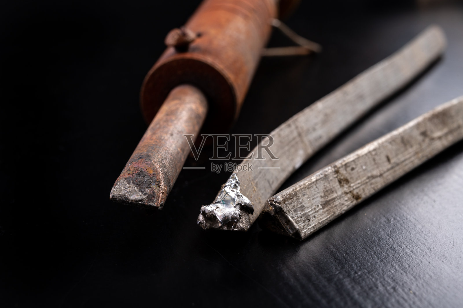 工作台上的大型烙铁和焊接配件。使用焊接连接板材。黑暗的背景。照片摄影图片