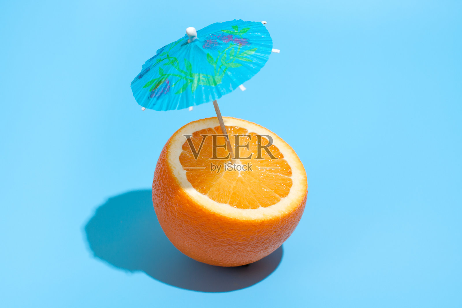 新鲜多汁的橙子和鸡尾酒伞孤立在蓝色的背景。健康饮食和节食的概念。饮料的概念照片摄影图片
