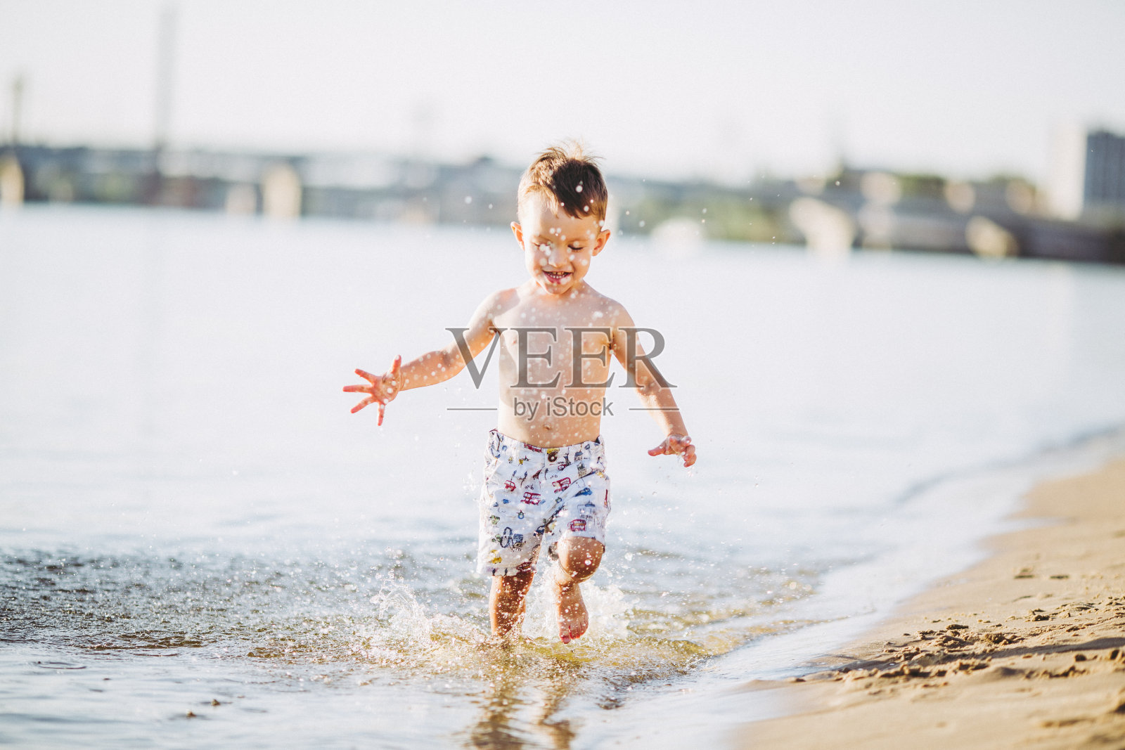 小男孩在河边玩,溅起水花,拍起手来照片摄影图片