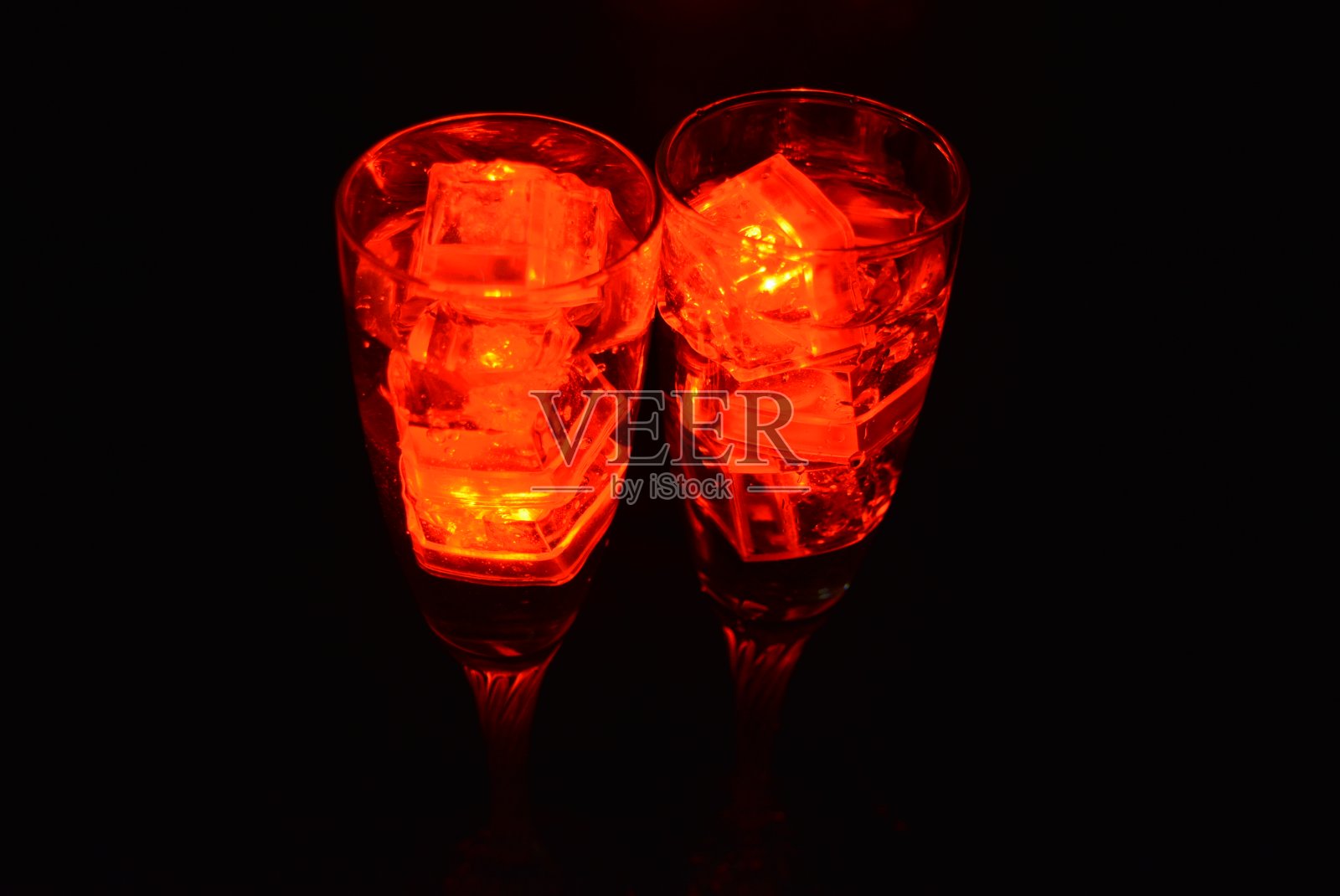 两杯不同寻常的香槟,一杯饮料和鲜红的冰片。在黑色的背景、令人印象深刻的照片和情人节的盛宴上,用塑料冰块照亮每个杯子里的饮料。照片摄影图片