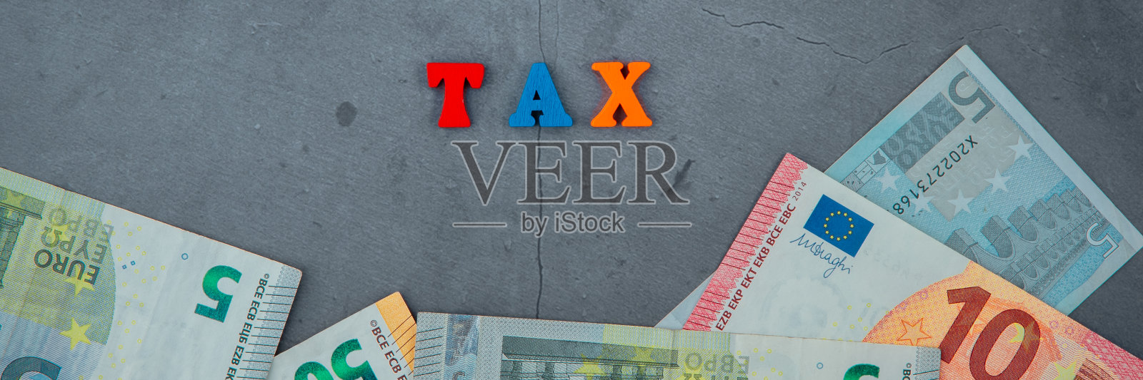 这个五颜六色的税收词是由灰色灰泥墙背景上的木制字母组成的。照片摄影图片