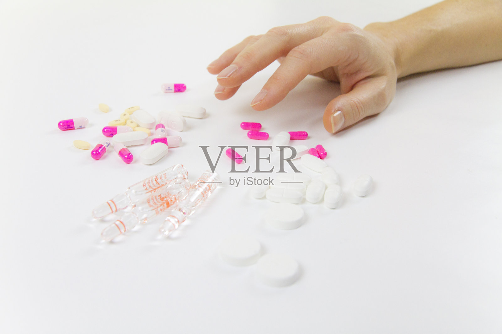 沉迷于药物和药物在现代:一个年轻女子的手即将抓取各种药片和小瓶在桌子上和白色的背景照片摄影图片