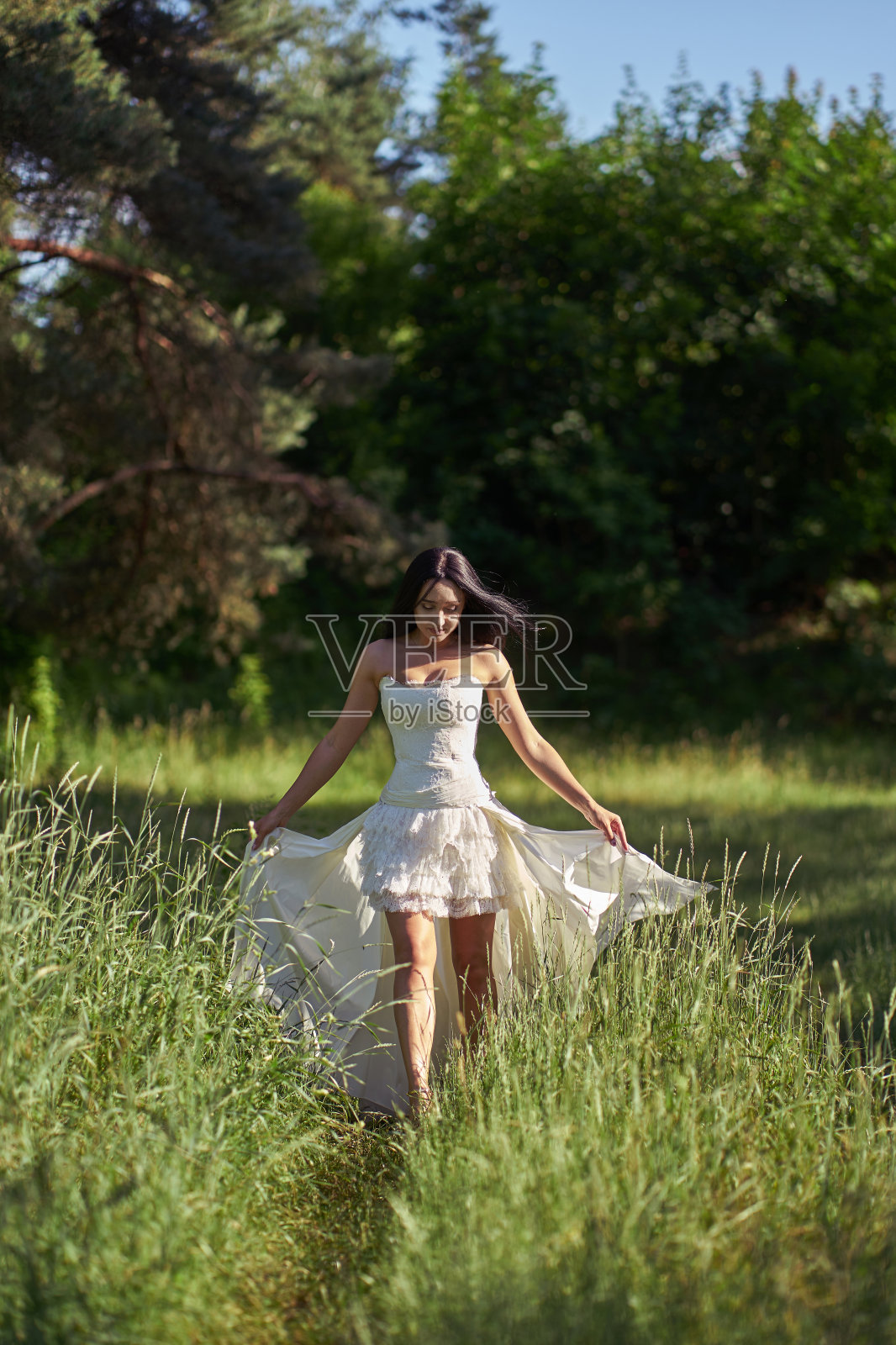年轻漂亮的黑发新娘微笑着穿着白色婚纱,走在户外照片摄影图片