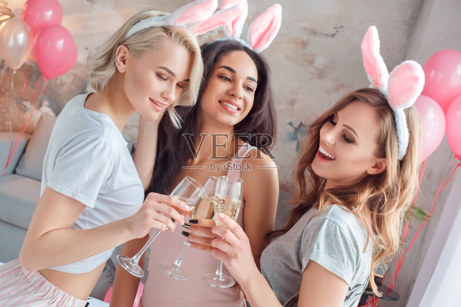 聚会,派对年轻女人戴着兔子耳朵一起在家里的床上喝香槟干杯快乐的特写照片摄影图片