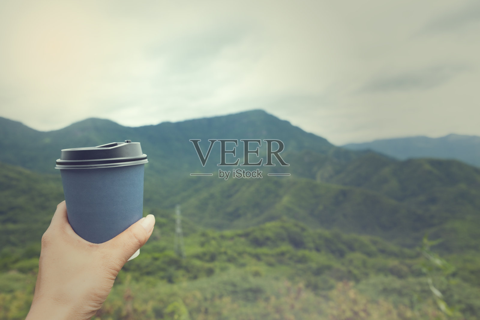 手握热咖啡杯,背景是山。照片摄影图片