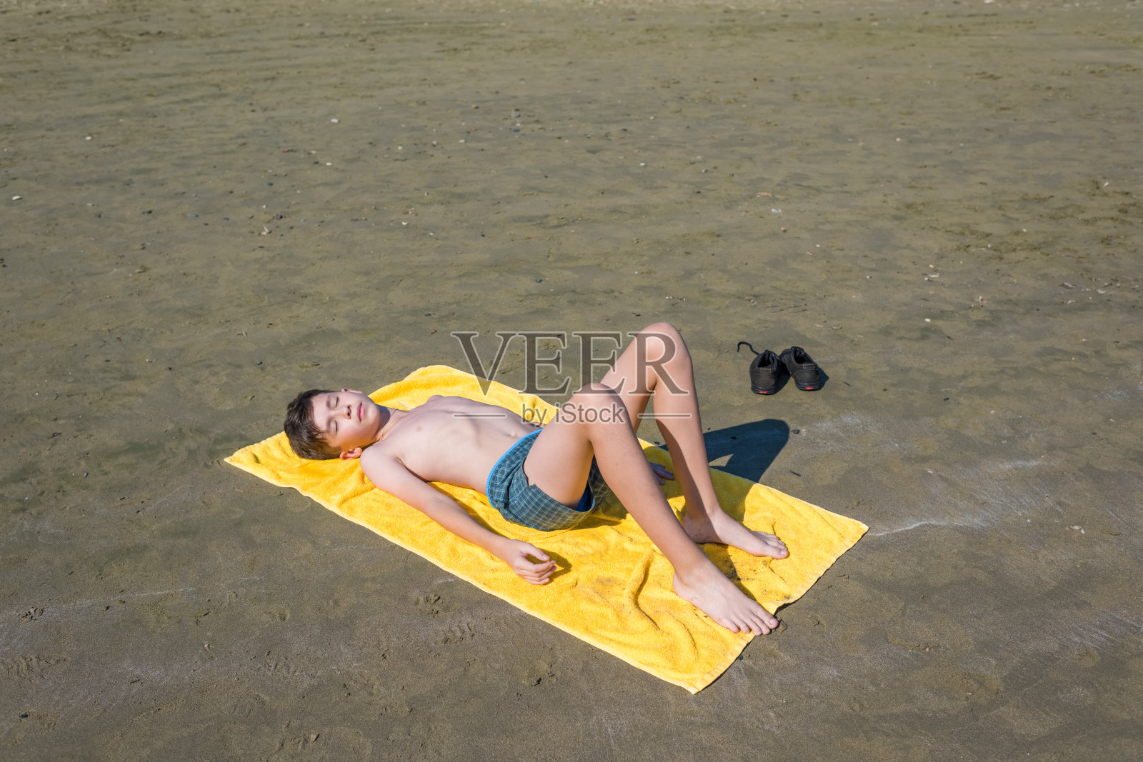 俯视图上的十几岁的男孩躺在黄色的毛巾和日光浴在海滩上。概念”nteen,男孩,游泳照片摄影图片