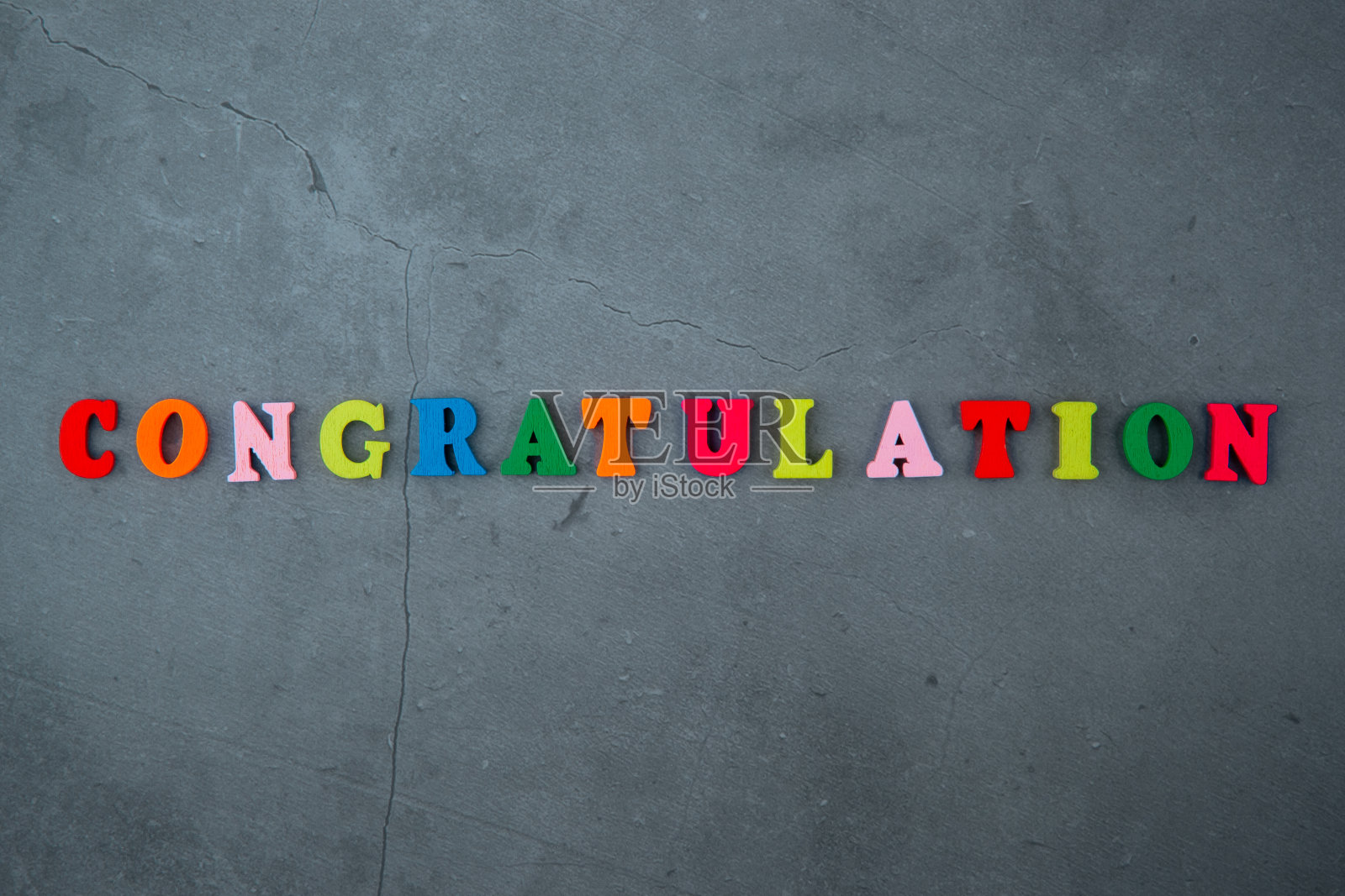 彩色的贺词是由木制字母组成的,背景是灰色的灰泥墙。照片摄影图片