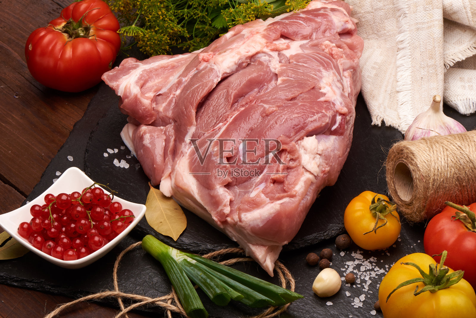 生猪肉放在石板石板上,配上香料、五颜六色的西红柿和红醋栗,以乡村的木头为背景。照片摄影图片