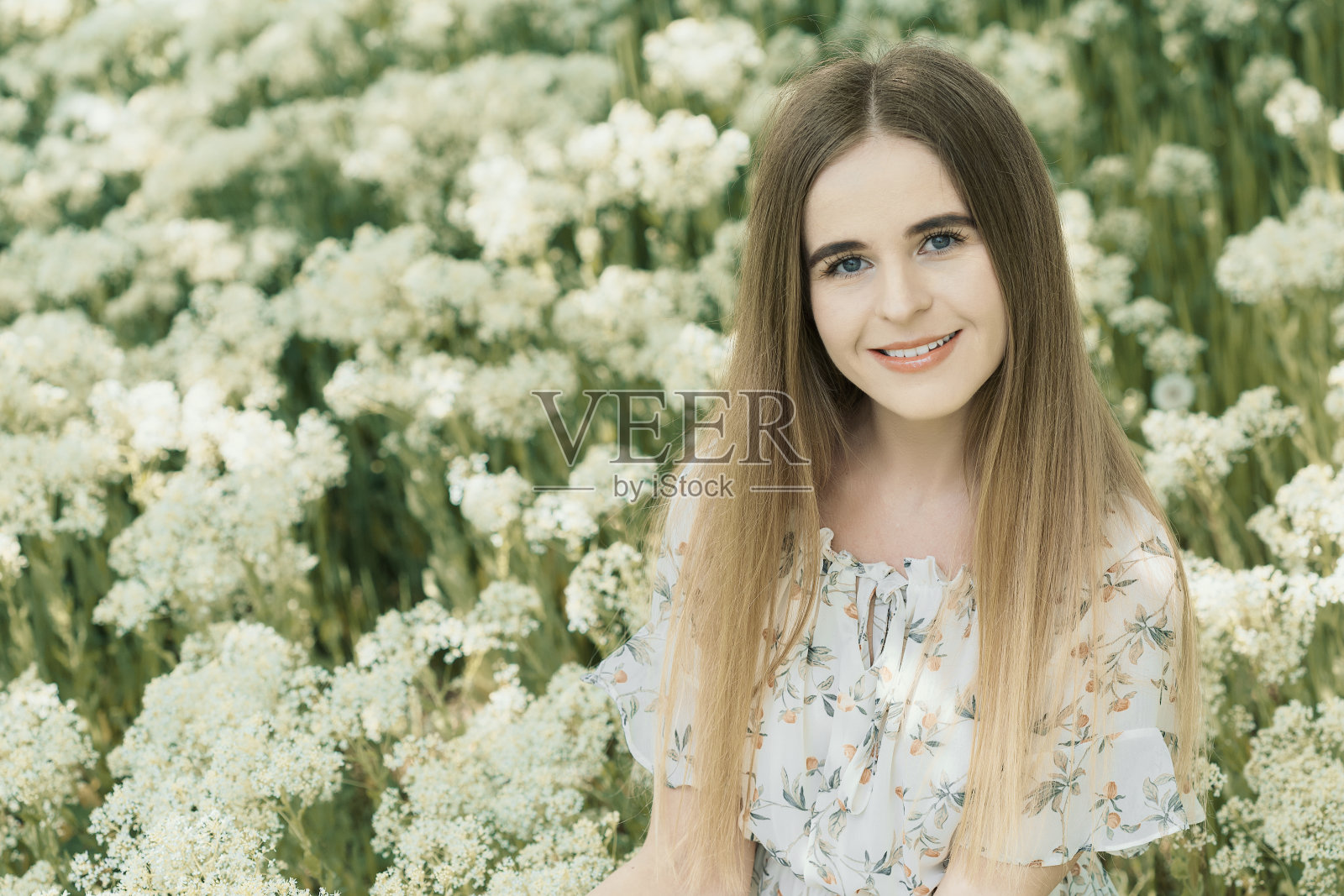 一个美丽的微笑的年轻女子的肖像与长金发在春天阳光灿烂的草地上盛开照片摄影图片