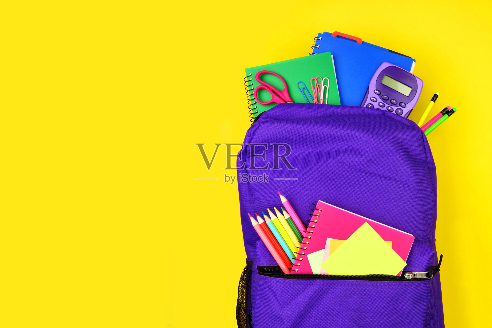 紫色的书包里装满了学习用品,背景是黄色,顶视图与副本空间照片摄影图片