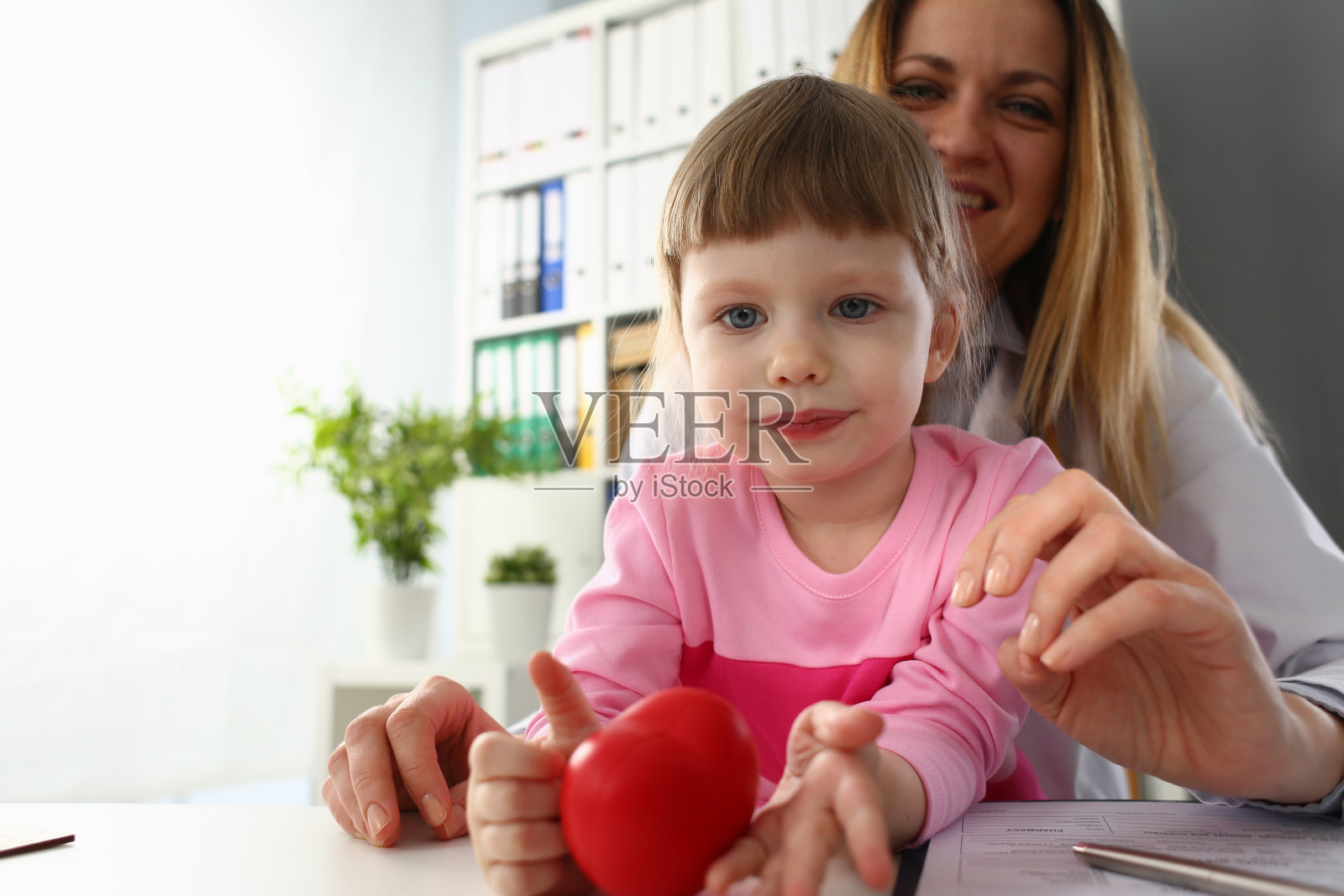 小女孩去看医生,手里拿着红色的玩具心脏照片摄影图片