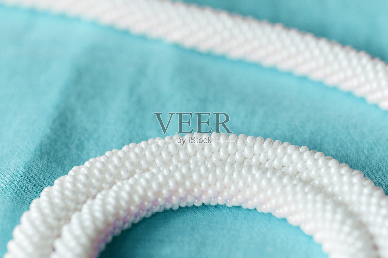 白色串珠项链上的蓝色纺织品背景近距离照片摄影图片