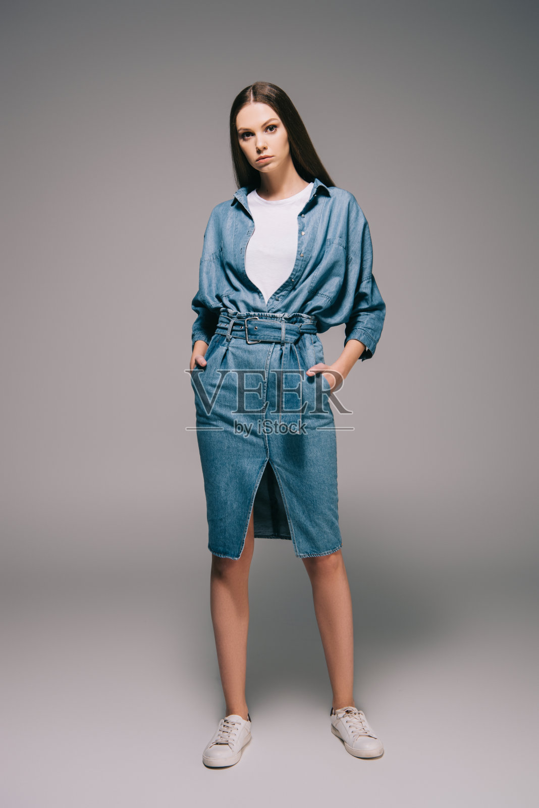 年轻的成年人和美丽的女人在牛仔裙与手在口袋看着相机照片摄影图片