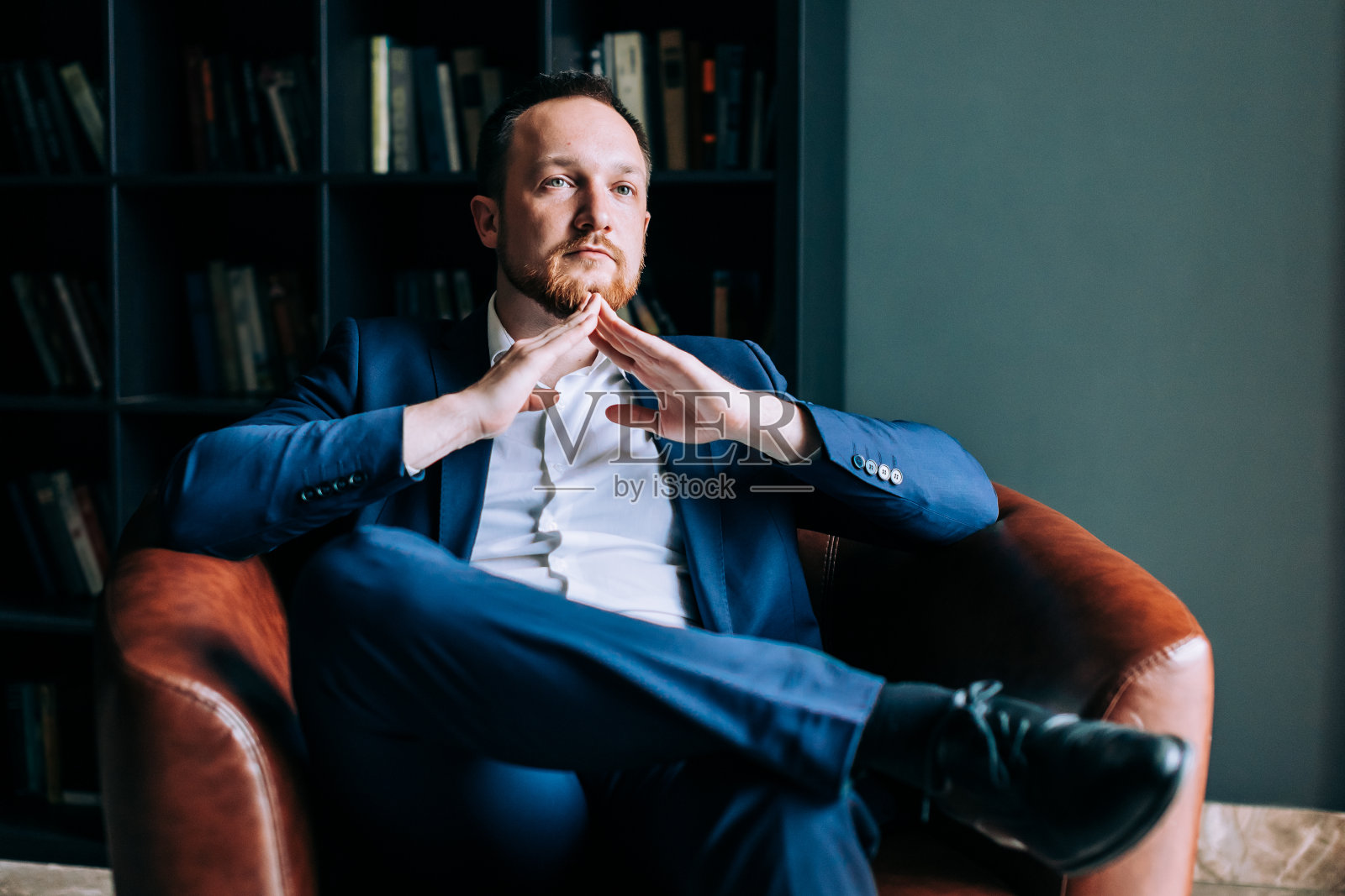 西装革面的成功商人双臂交叉坐在椅子上。照片摄影图片