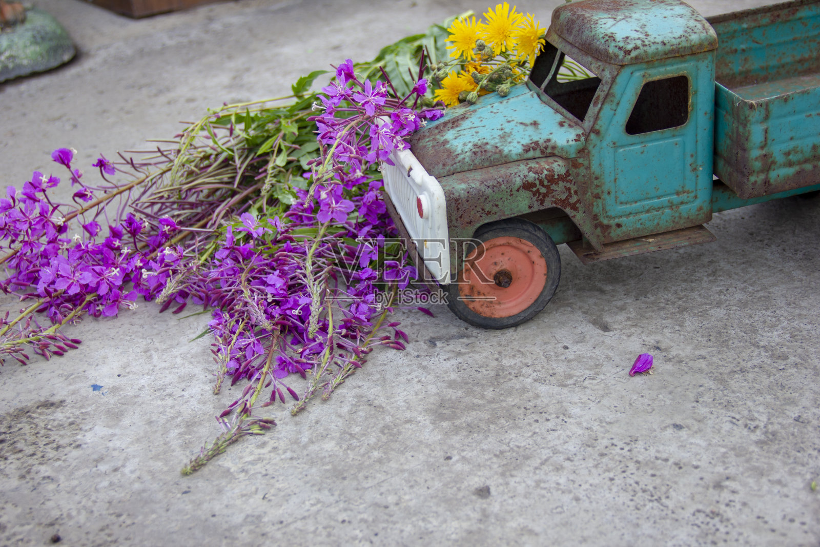 混凝土上有腐蚀痕迹的玩具金属机器。机器的压盖生锈。照片摄影图片