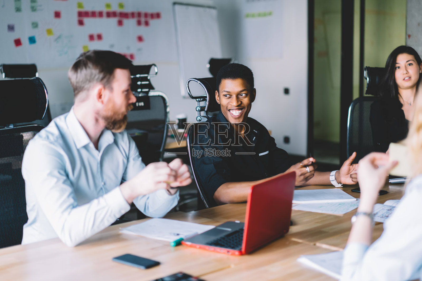 来自不同文化背景的员工穿着正装坐在会议桌前讨论设计项目。由不同的mae和女性专业人员组成的团队在简报期间协作照片摄影图片