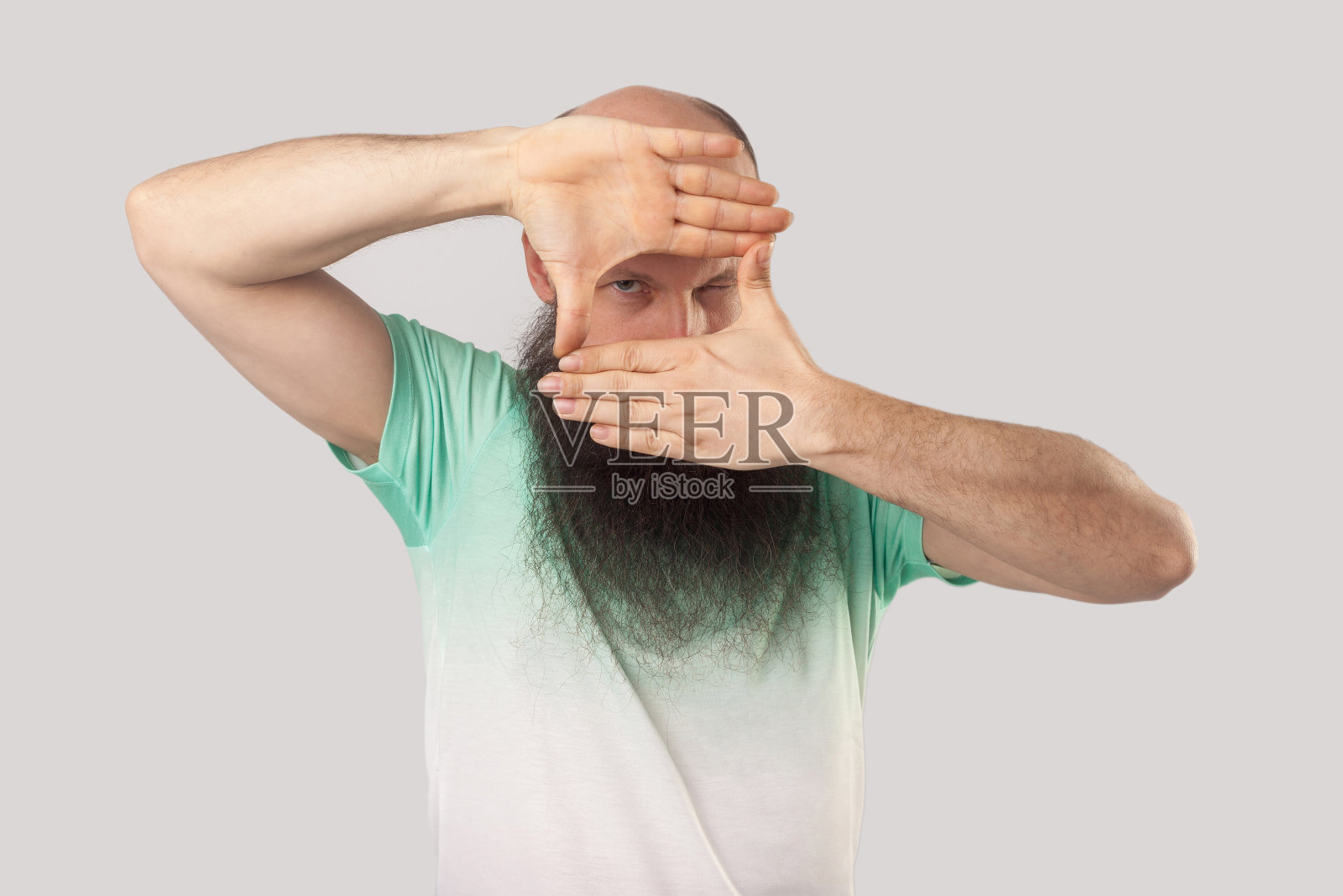 穿着浅绿色T恤,用手取景的专注中年秃顶长胡子男人肖像照片摄影图片